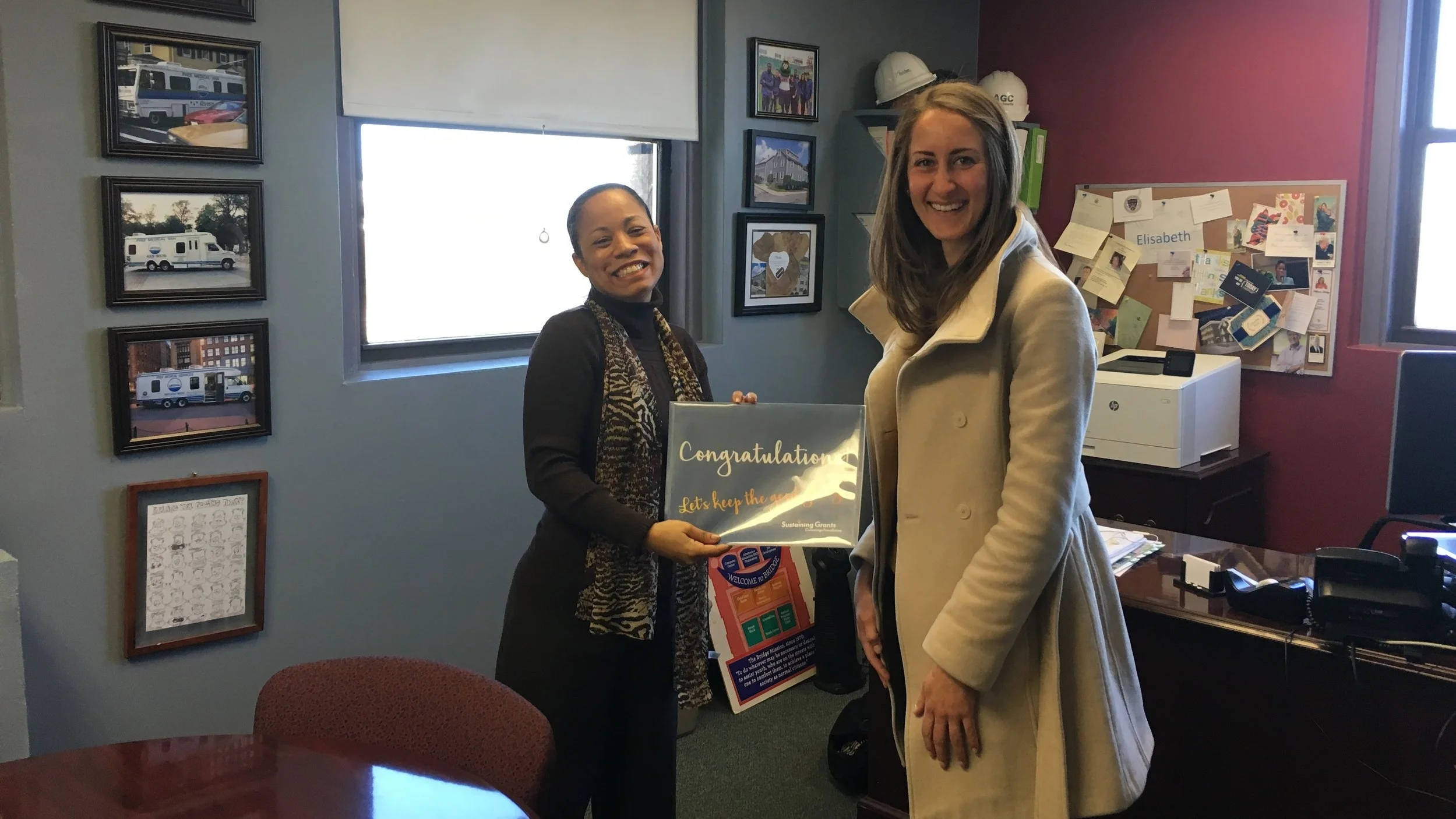Bridge Over Troubled Waters Executive Director Elisabeth Jackson (left) receives the exciting news and hand delivered award from Kathryn Jendrick of Cummings Foundation (right).