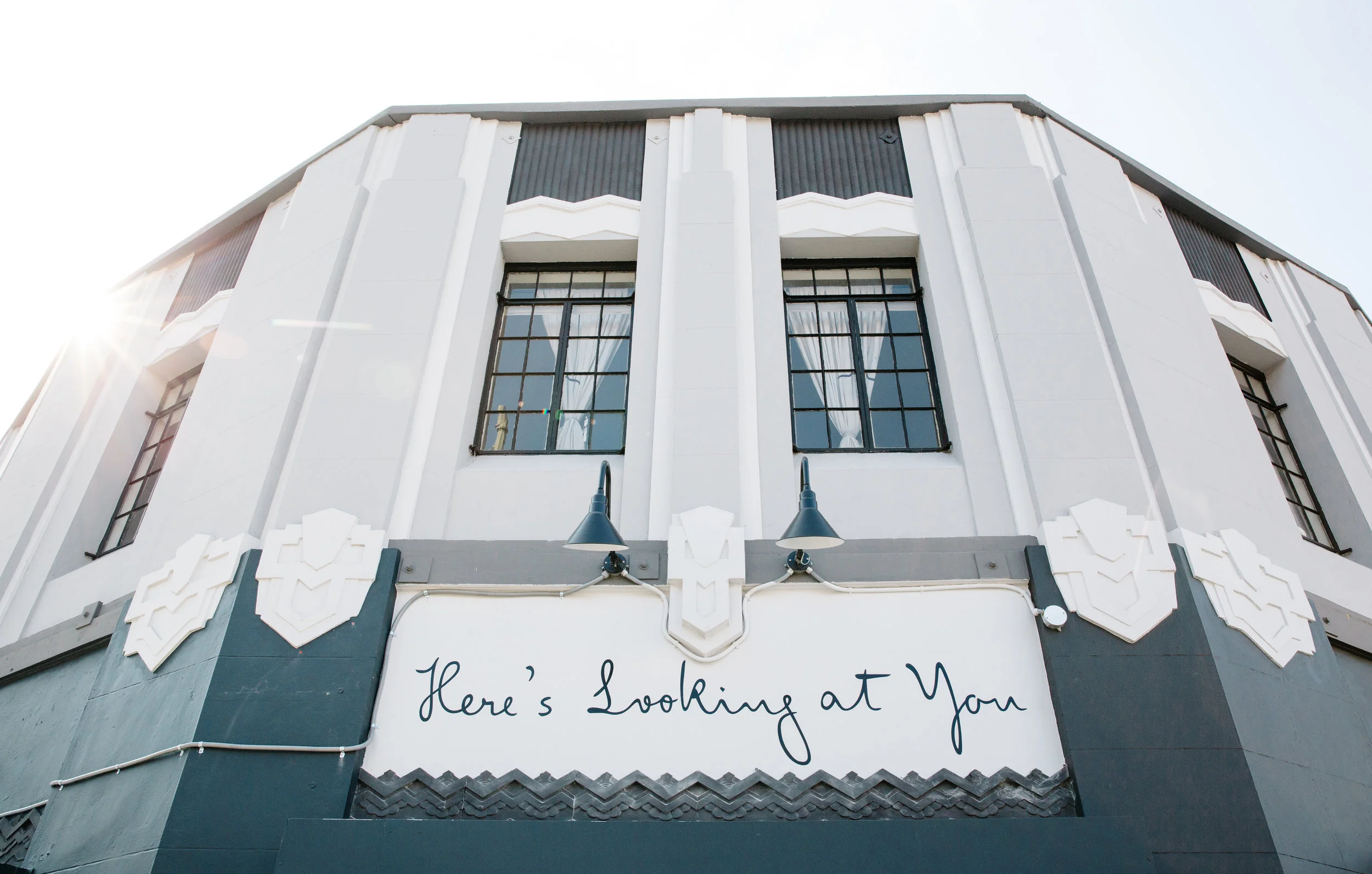 Image depicts the outside of the restaurant where it’s name “Here’s Looking at You” is scrawled in a dark teal script.
