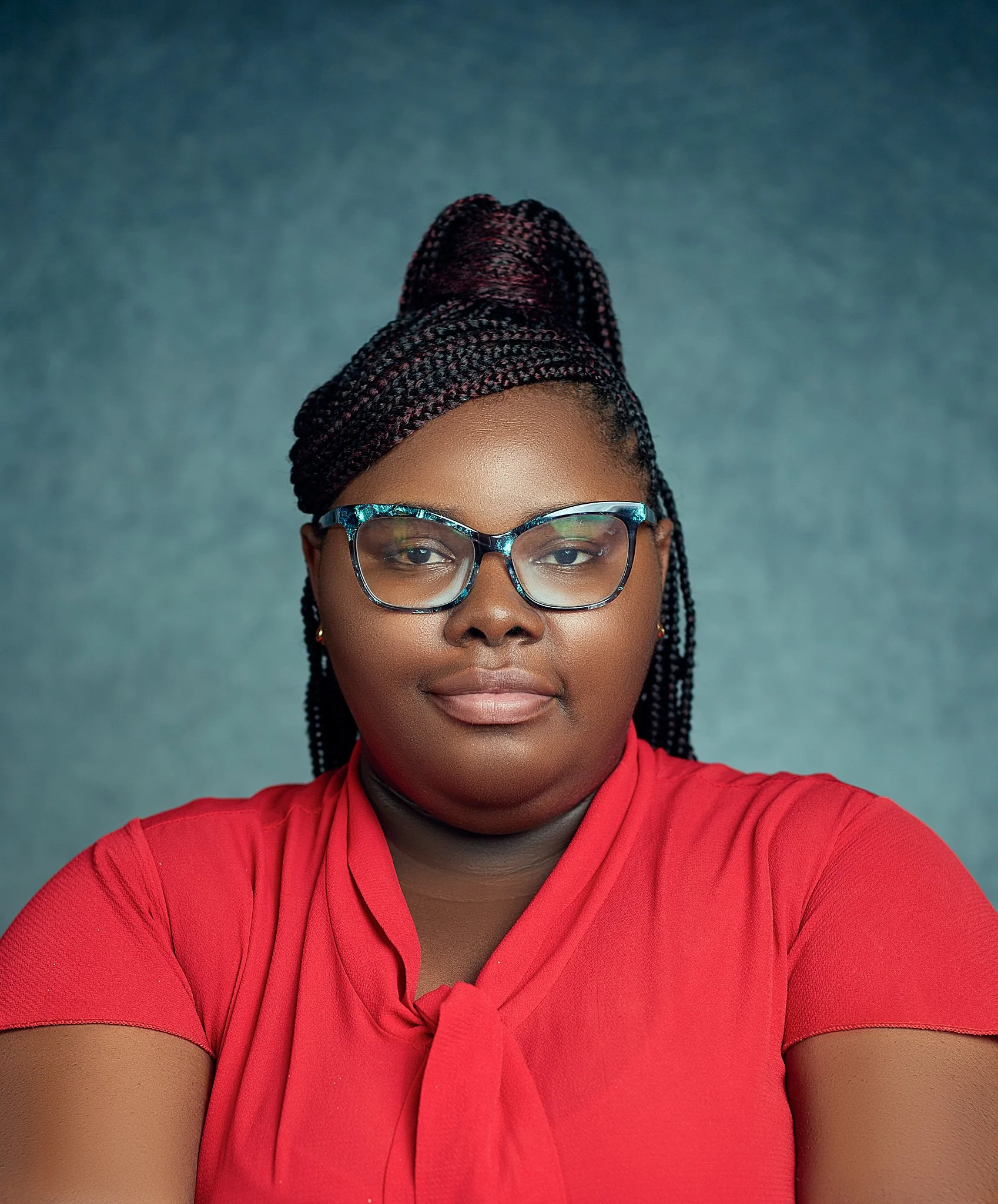 Portrait of a woman wearing glasses and a red top against a gray background.