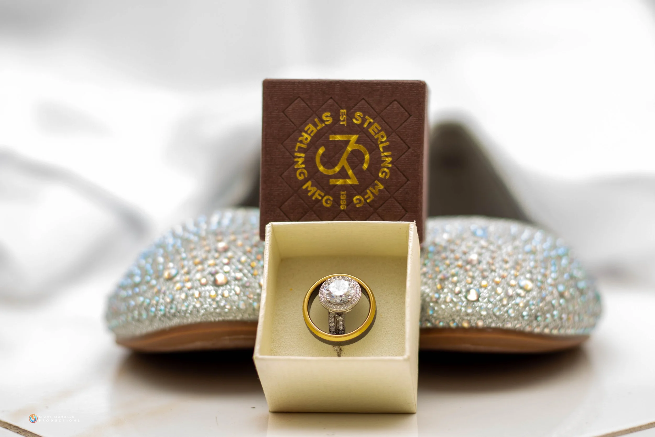 Diamond ring in a beige box, with a sparkly shoe and a wooden box in the background.