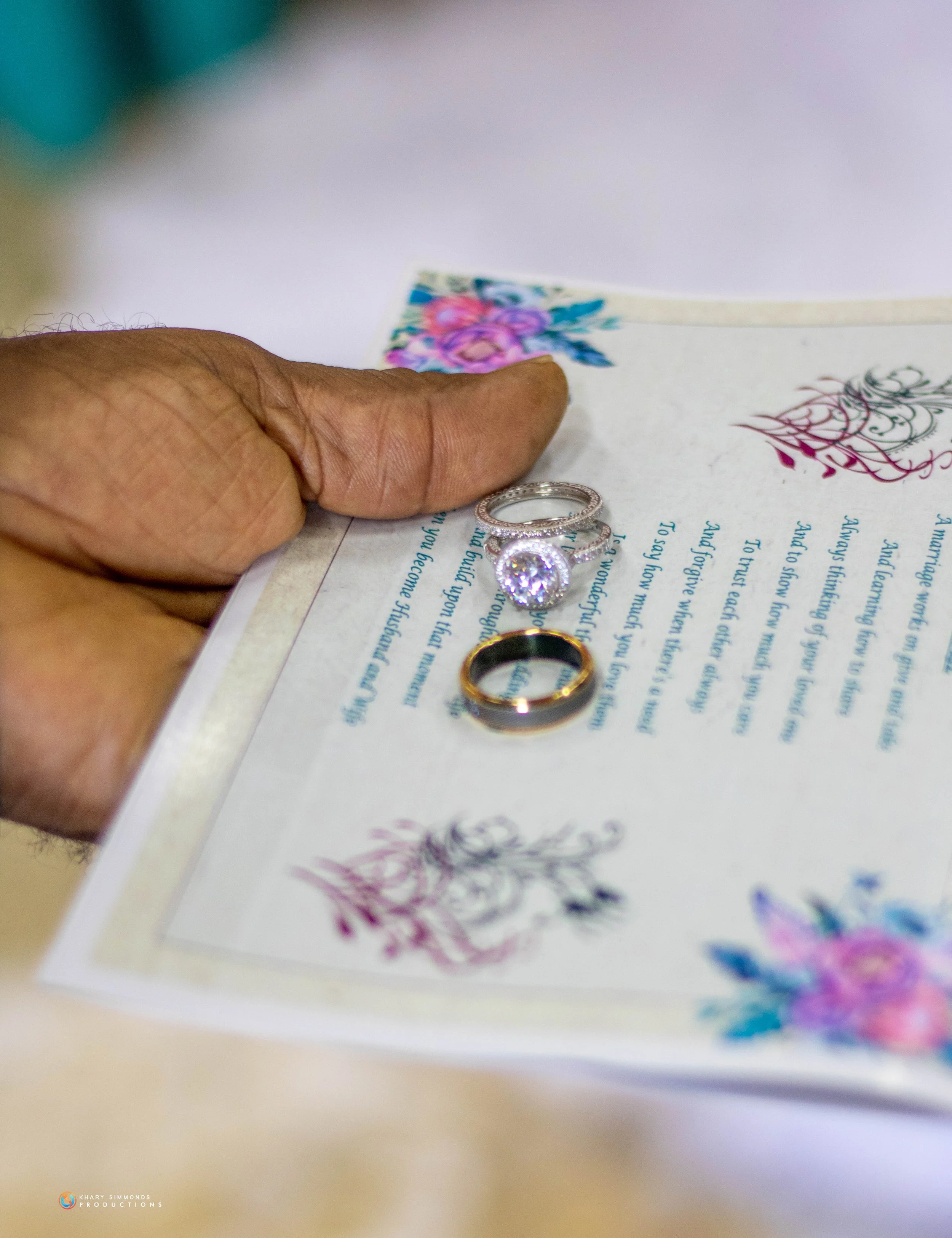 Close-up of a hand holding a wedding vow booklet with three rings resting on it.