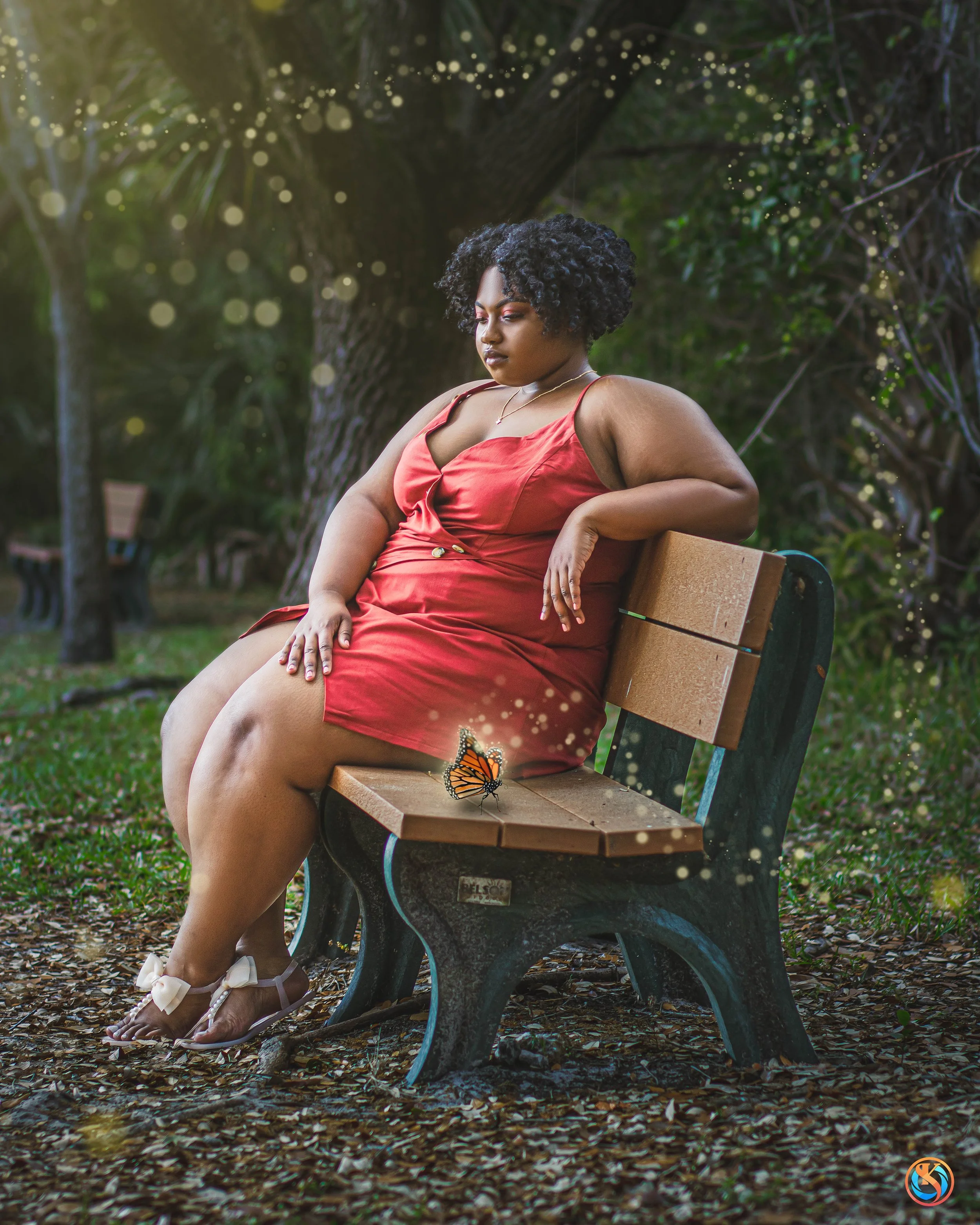 A woman in a red dress sitting on a park bench outdoors, with a butterfly resting on the bench nearby.