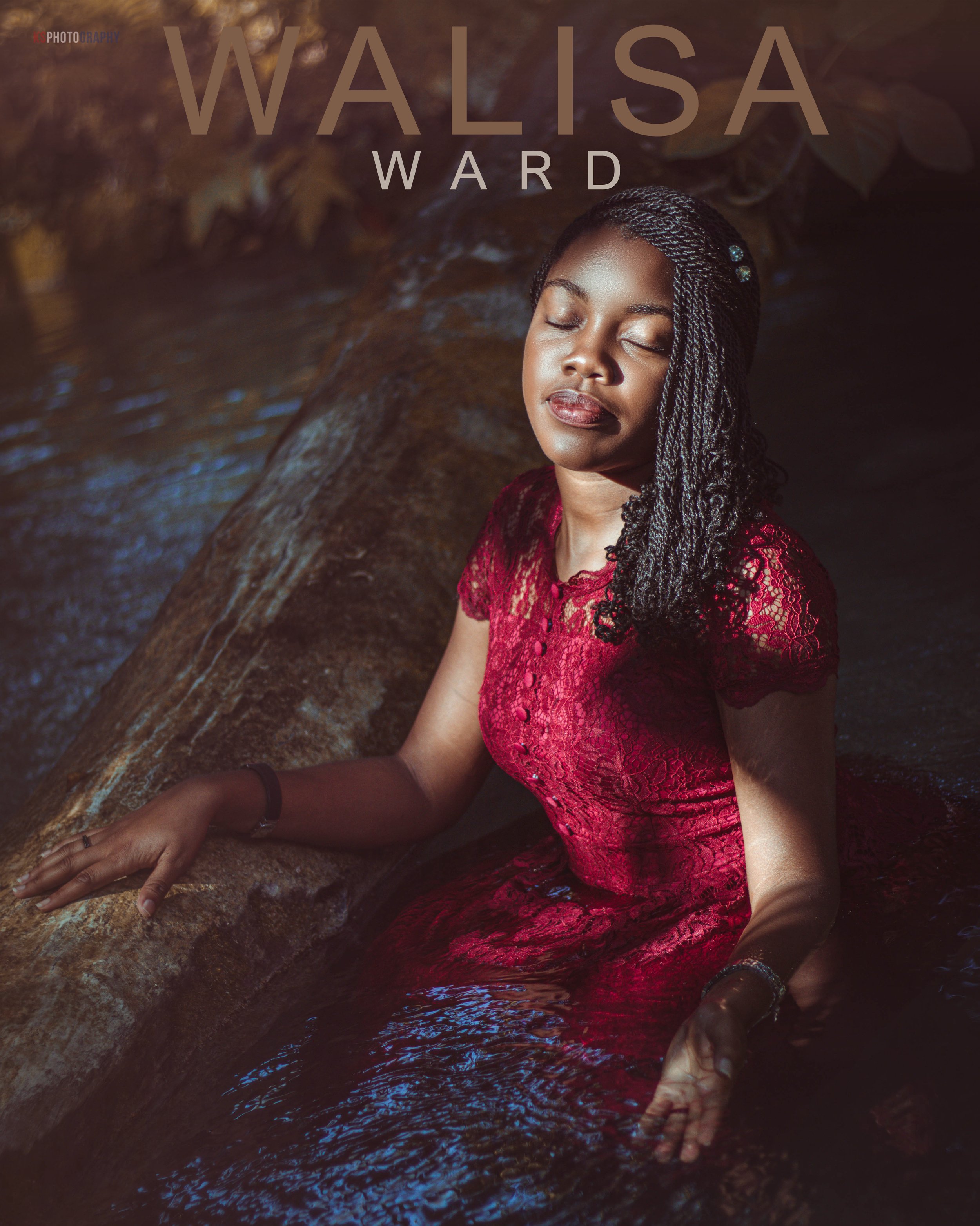 A woman with braided hair and a burgundy lace dress sitting in water with her eyes closed and a peaceful expression.