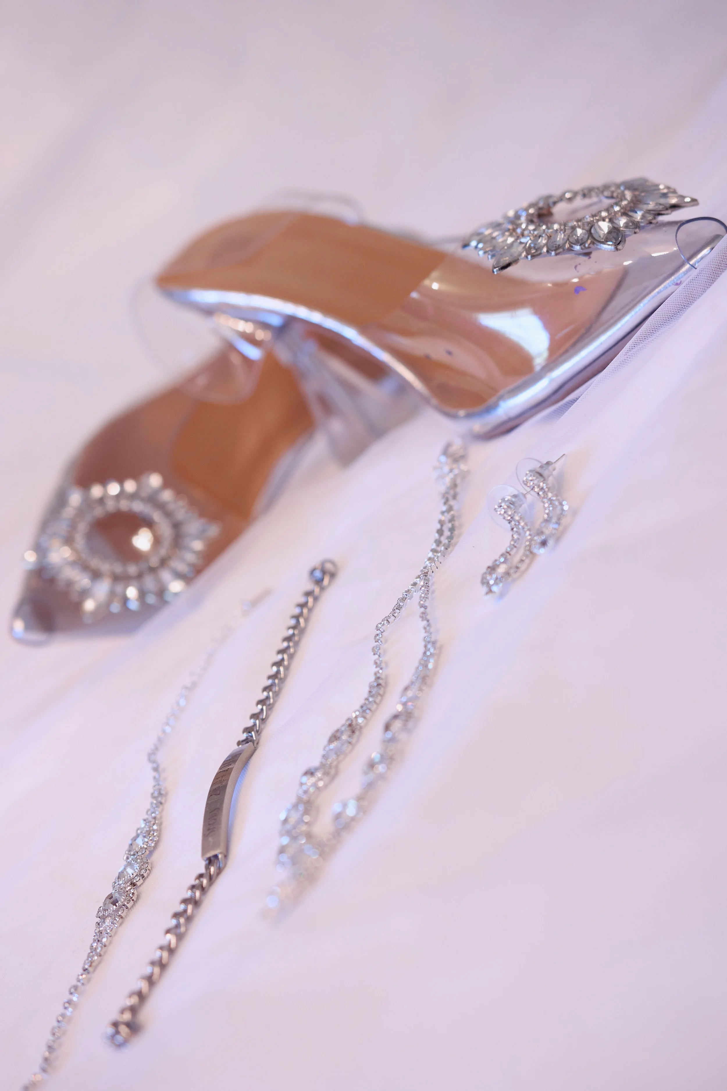 A collection of silver jewelry including necklaces, earrings, and bracelets, displayed on a white fabric, with a mirrored display stand.