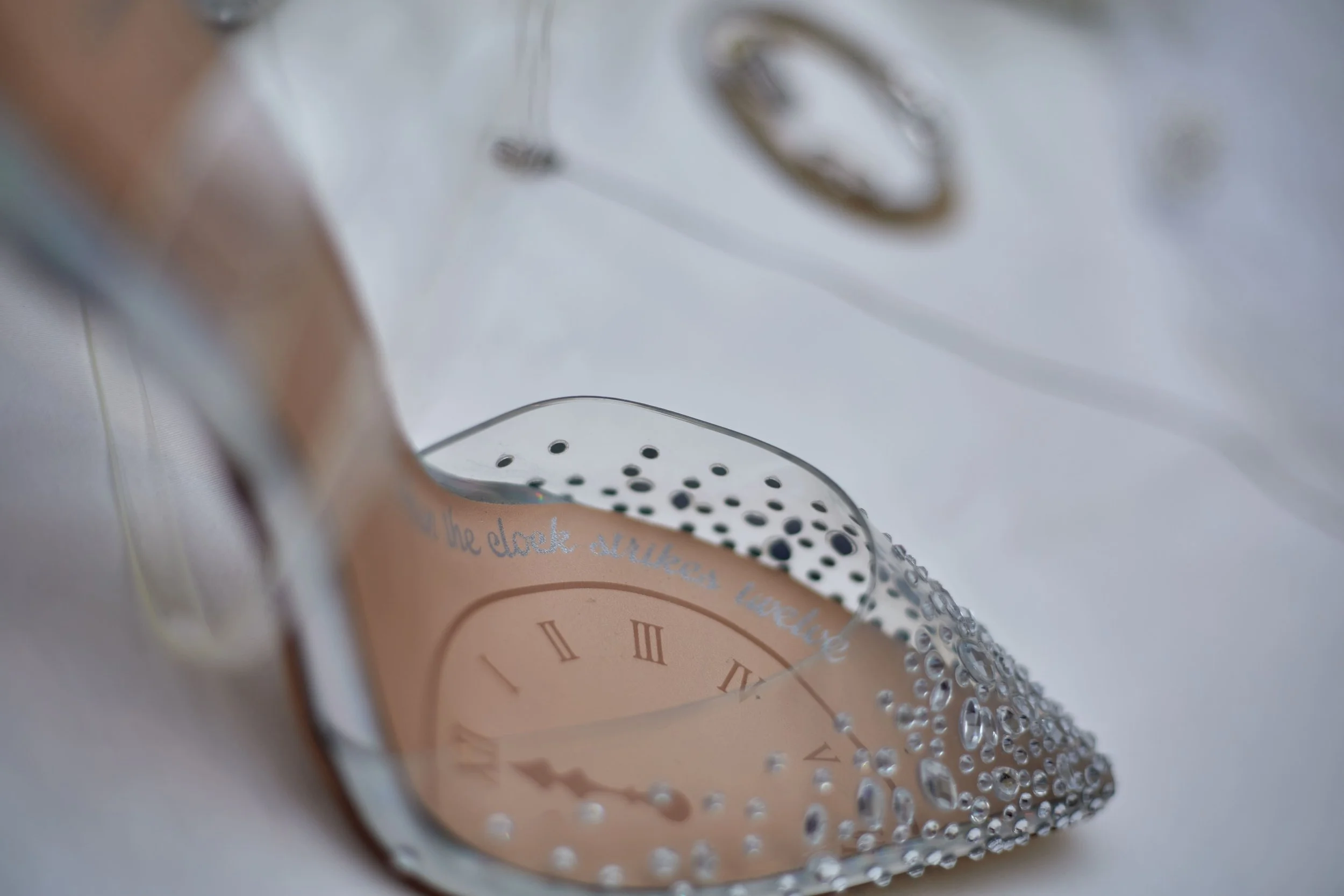 Close-up view of a glass clock ornament with water droplets, featuring Roman numerals and a reflection of a phrase that begins with 'The clock strikes...'