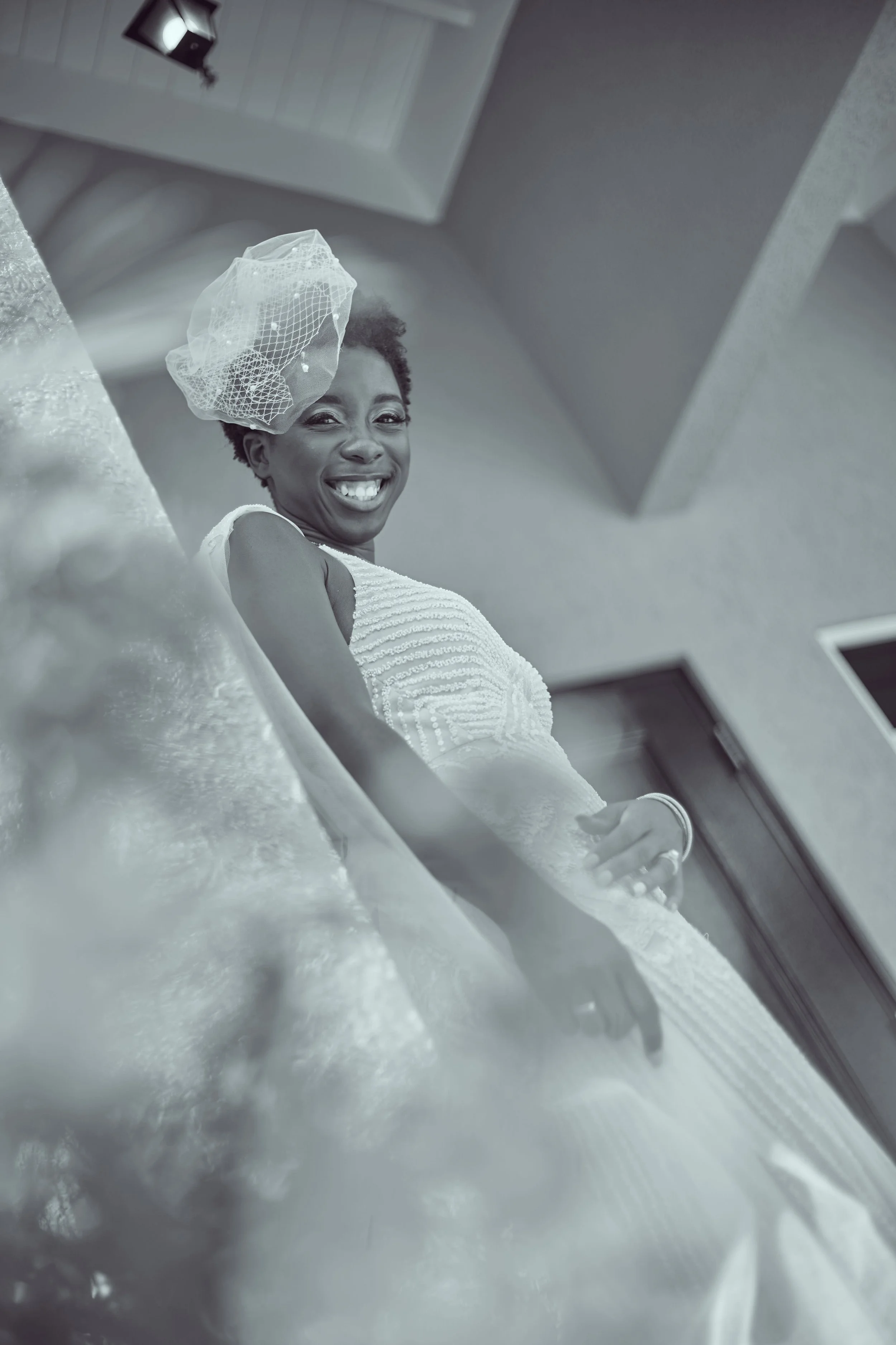 Smiling woman in a wedding dress with a veil, posing indoors. Black and white photograph.