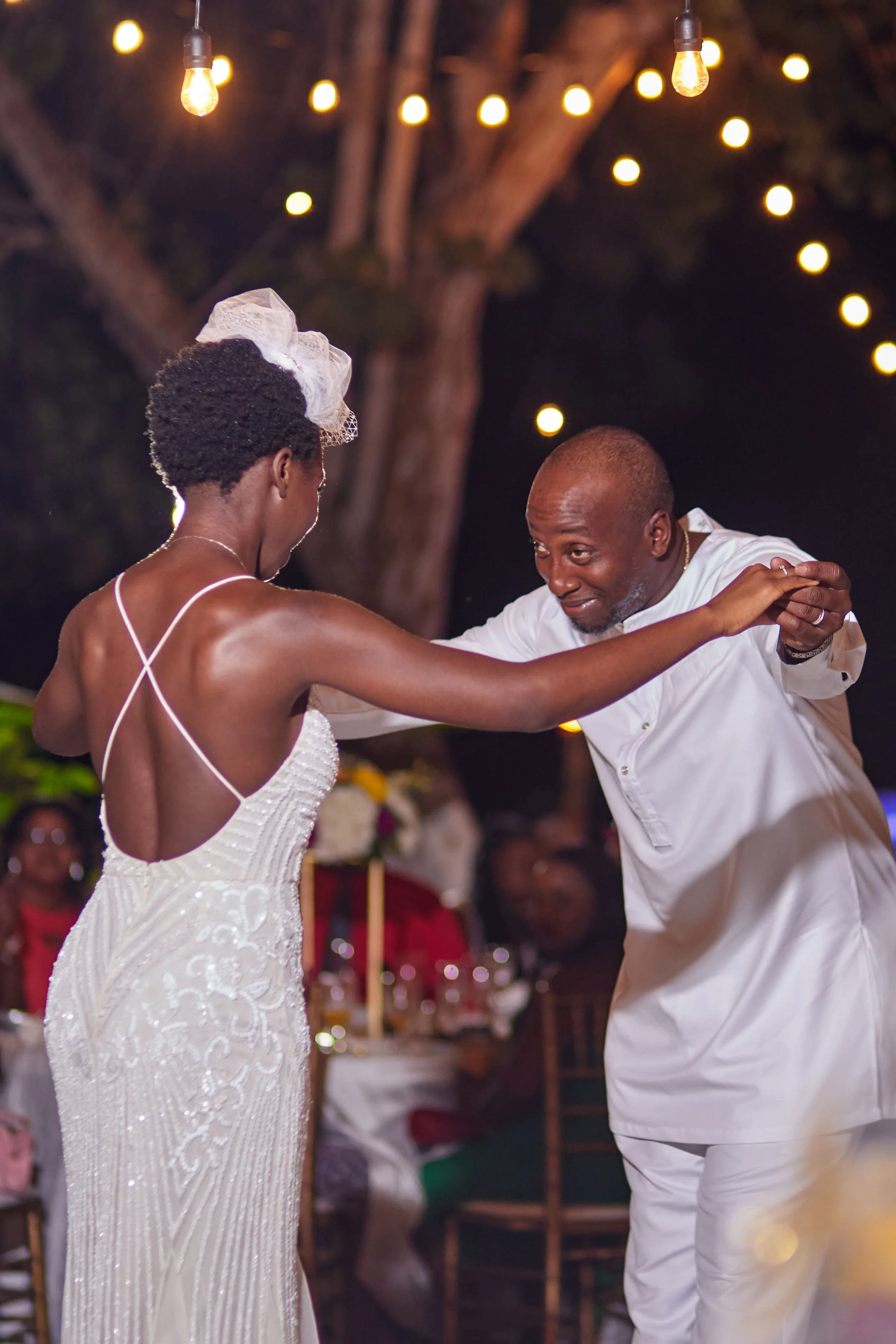 A couple dancing at an outdoor wedding reception at night with string lights overhead.