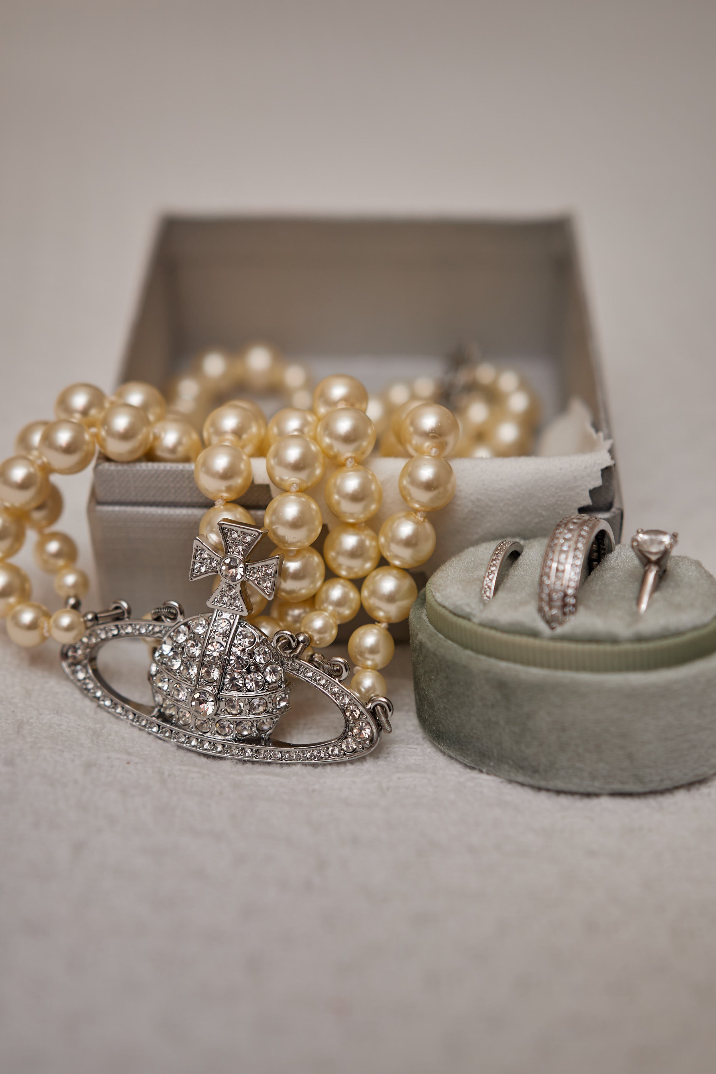 Pearl necklace, diamond rings, and a jeweled brooch in a jewelry box and display stand.