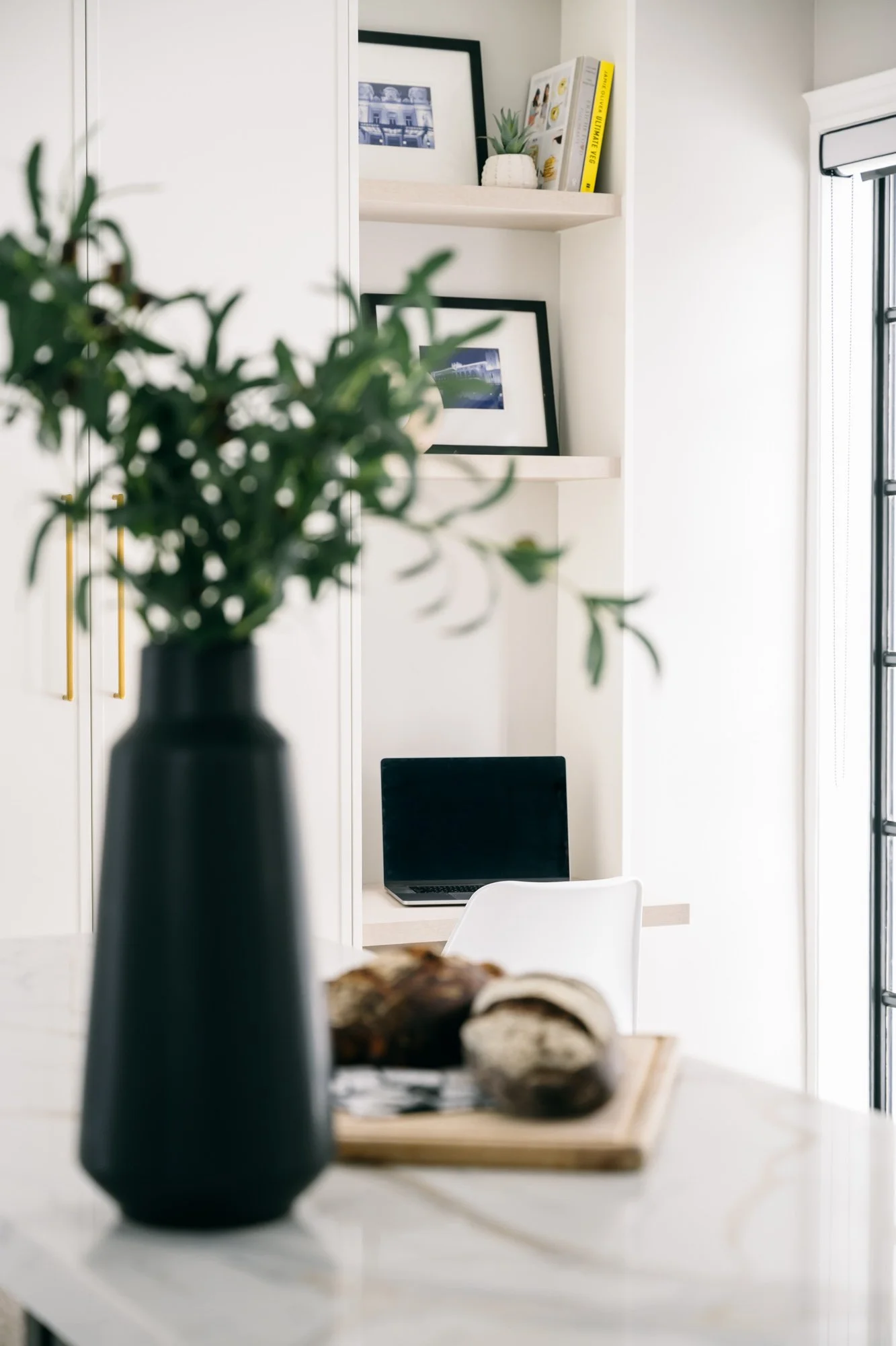 A laptop sits in a nook in a kitchen with built-in shelves above.