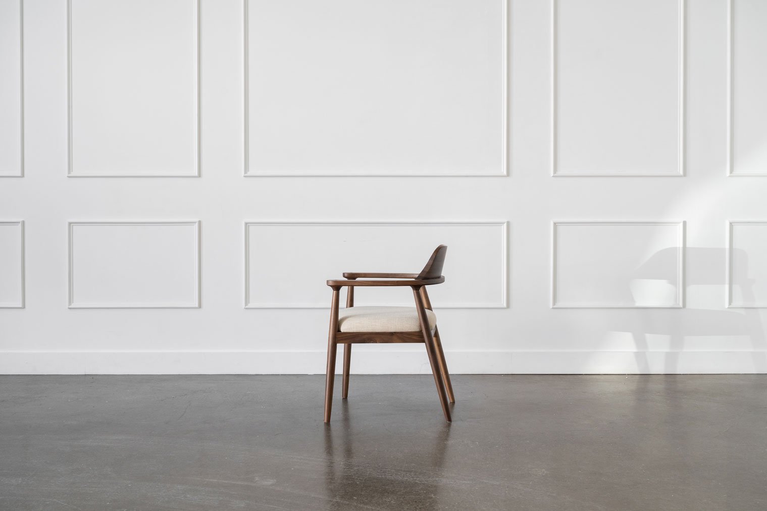 A side view of Mim Concept's brown Sophie dining chair sits in a large empty room.