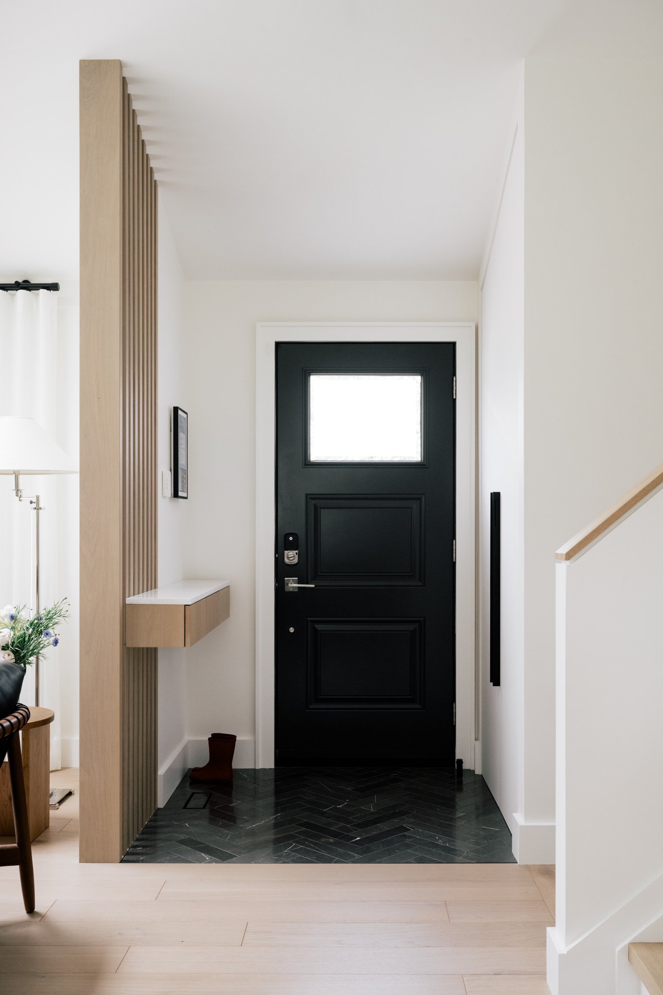 Black front door of an entryway. A custom built floating shelf is attached to the slat room divider of the entryway.