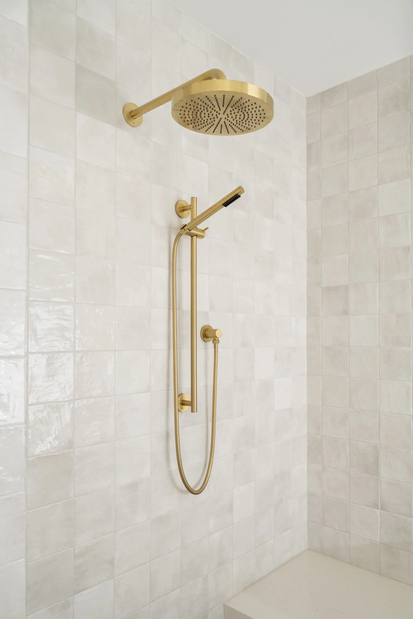 Gold shower head and waterfall shower in a shower with square tile.