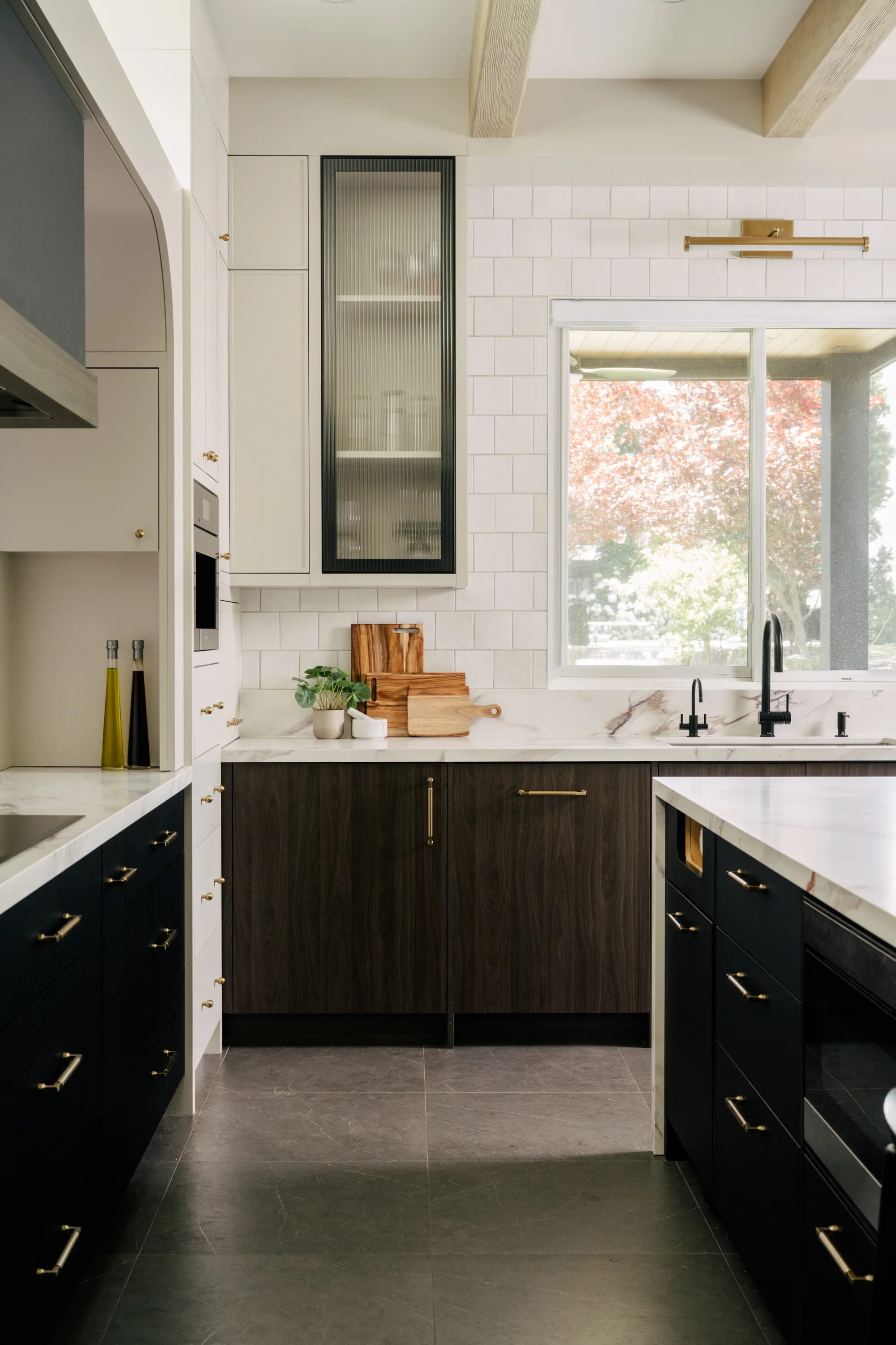 A galley view of the a tall kitchen with dark brown and black lower cabinets. Wood boards sit on the countertop, against the tiled wall.