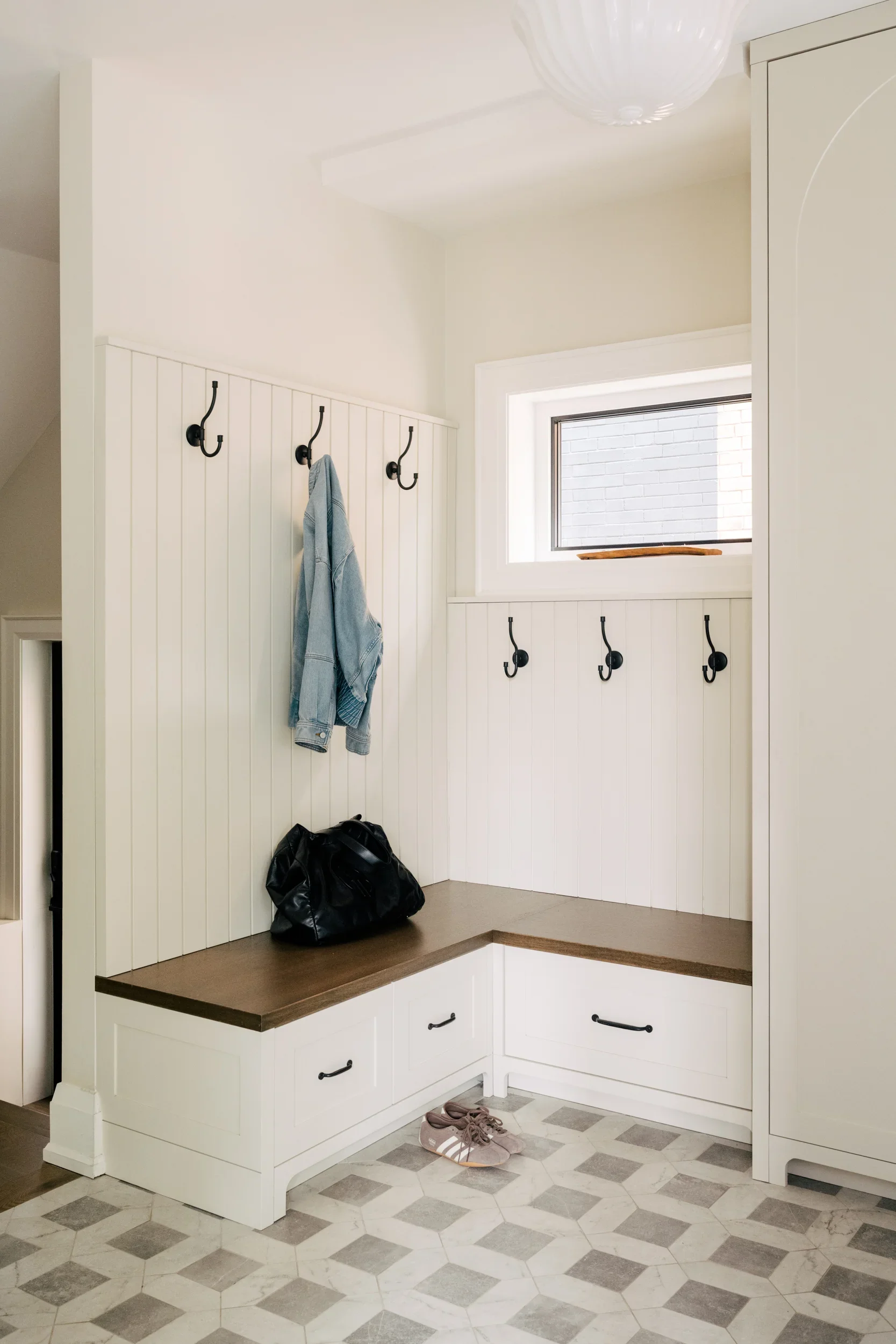 Foyer in a home with hooks on the wall and a built-in bench. A purse sits on the bench and a jean jacket hangs on one of the wall hooks.