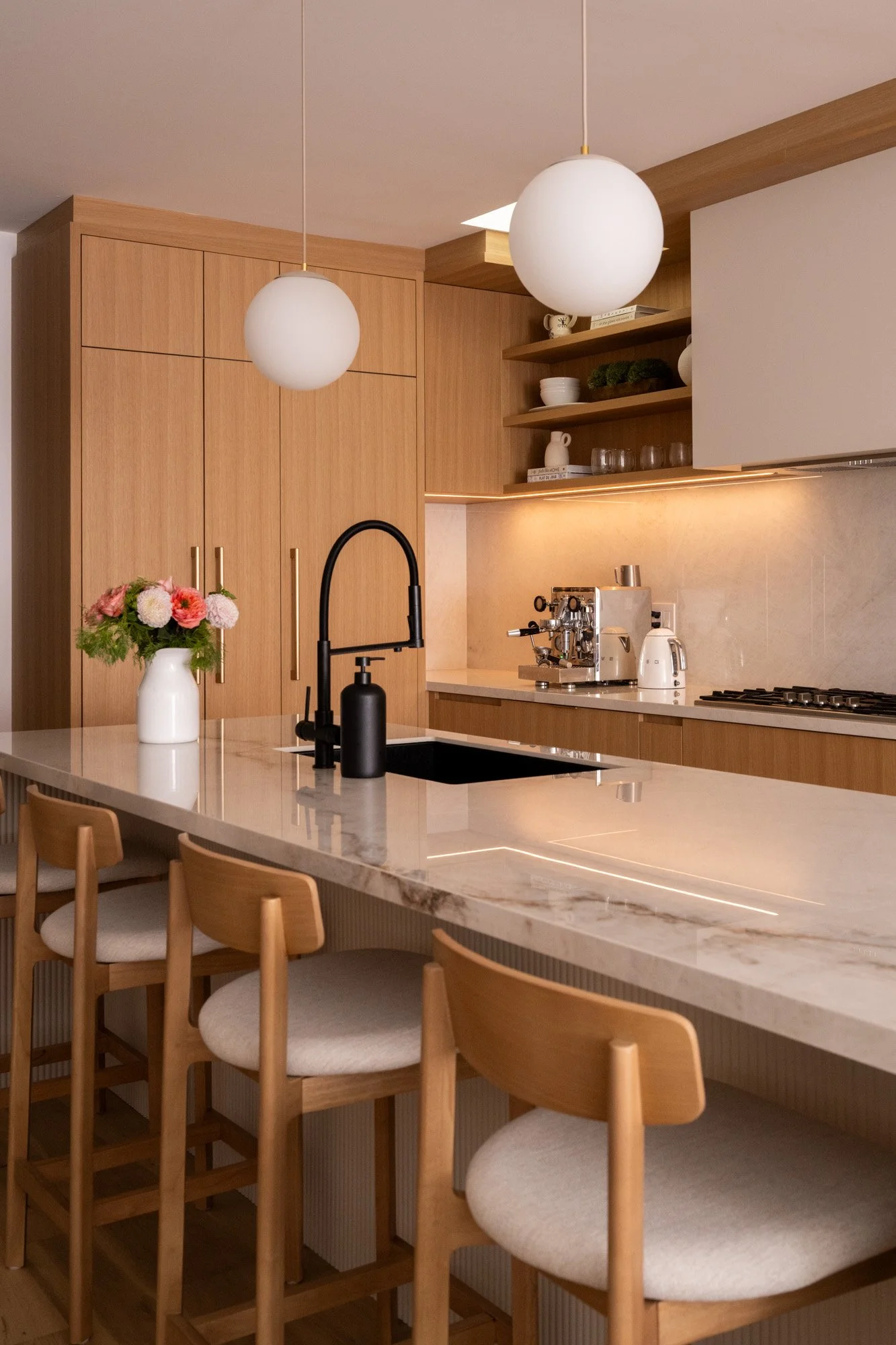 A vase of flowers sit on top of a large reeded kitchen island. Under cabinet lights are turned on