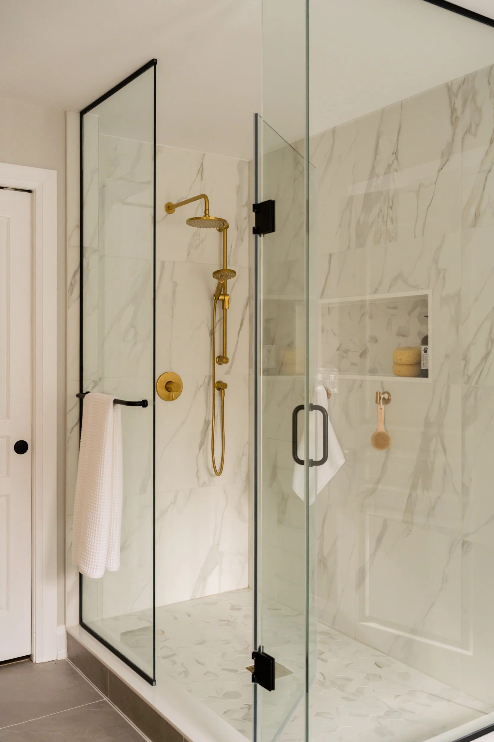 A large freestanding shower with a glass door, gold hardware and a wall niche.
