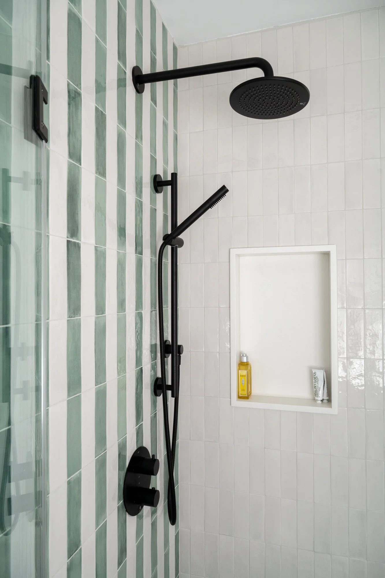 A shower with white and green striped wall tile, matte black shower hardware, and a shower niche.