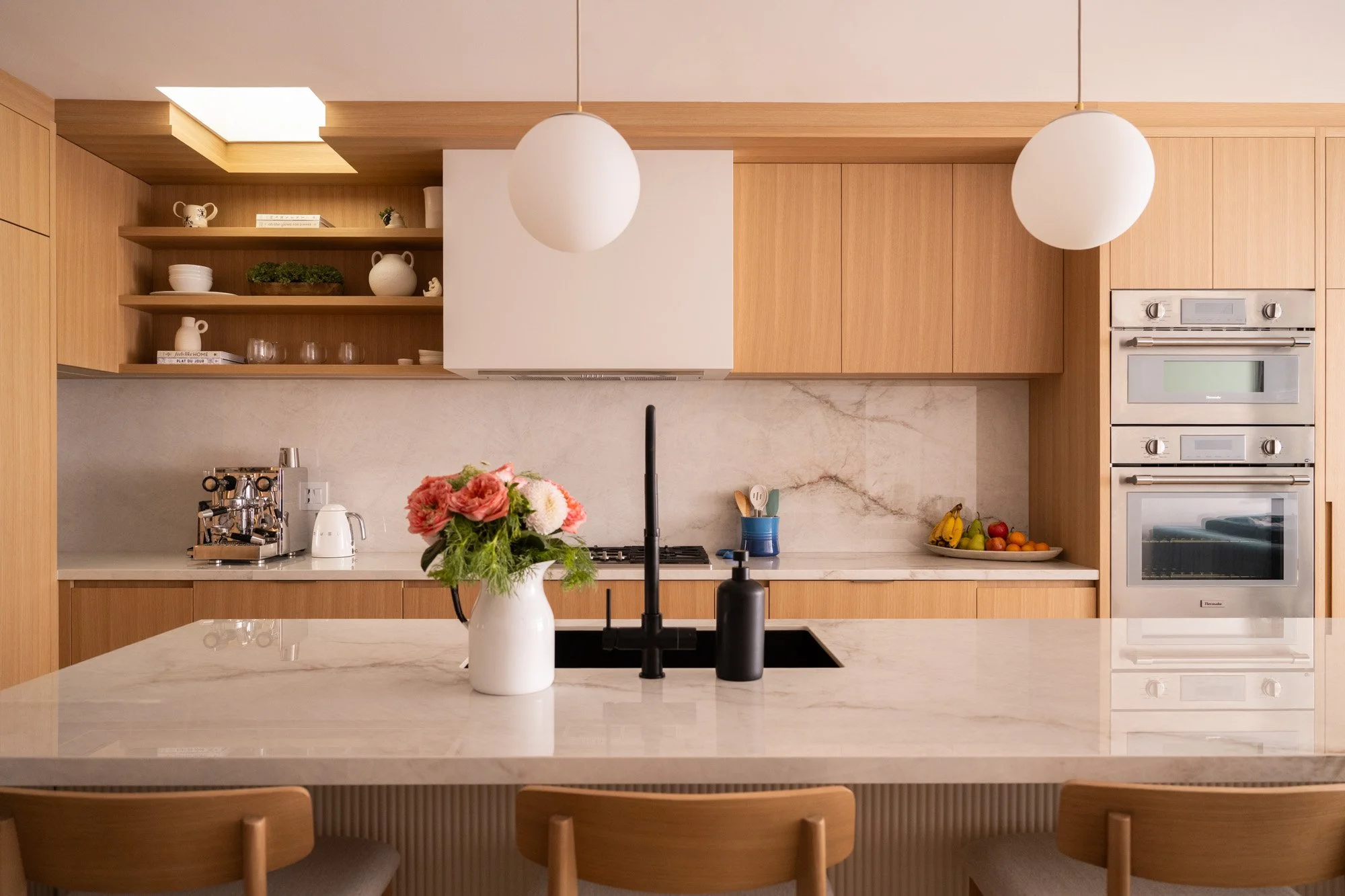 A large kitchen spans from left to right with open upper shelves on the left and integrated ovens on the right.