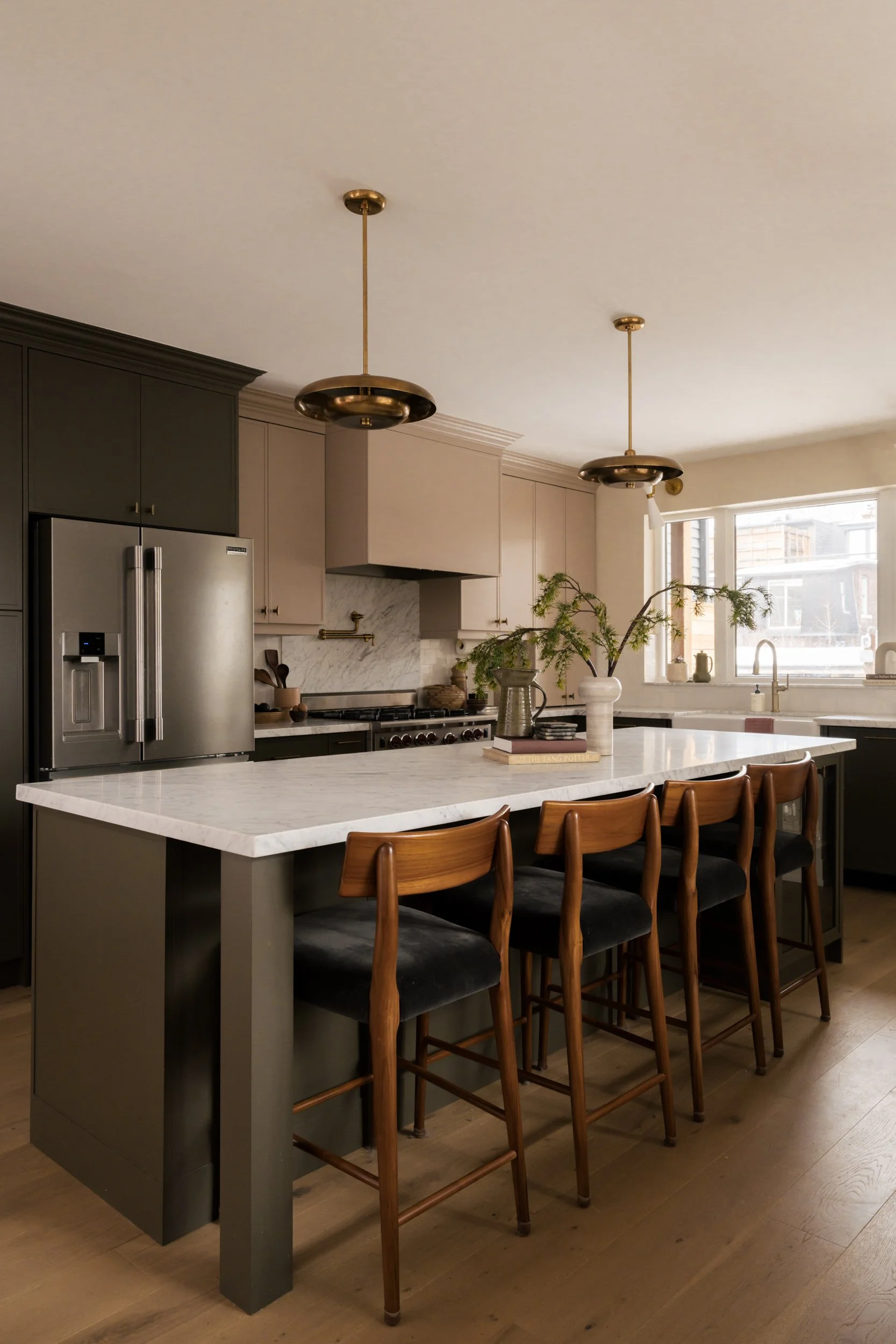 Long kitchen island with 4 wooden stools in a large kitchen. Two pendants hang from the ceiling above.