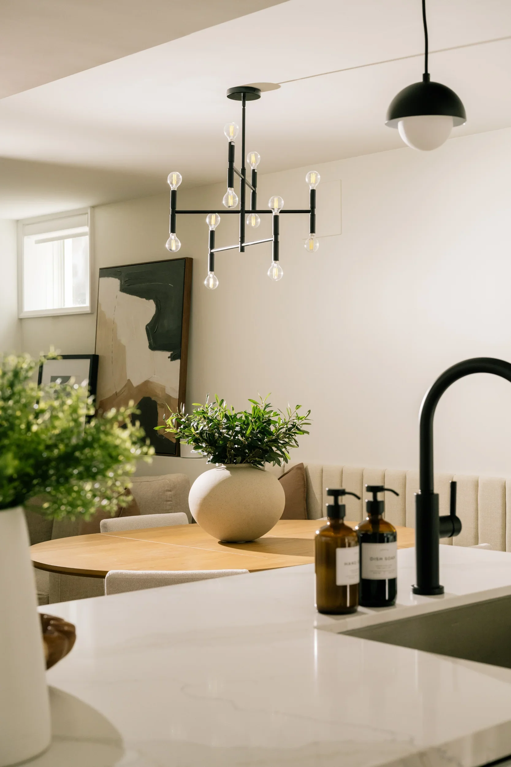 A large round vase with greenery sits on a dining table with dramatic lighting from the left.