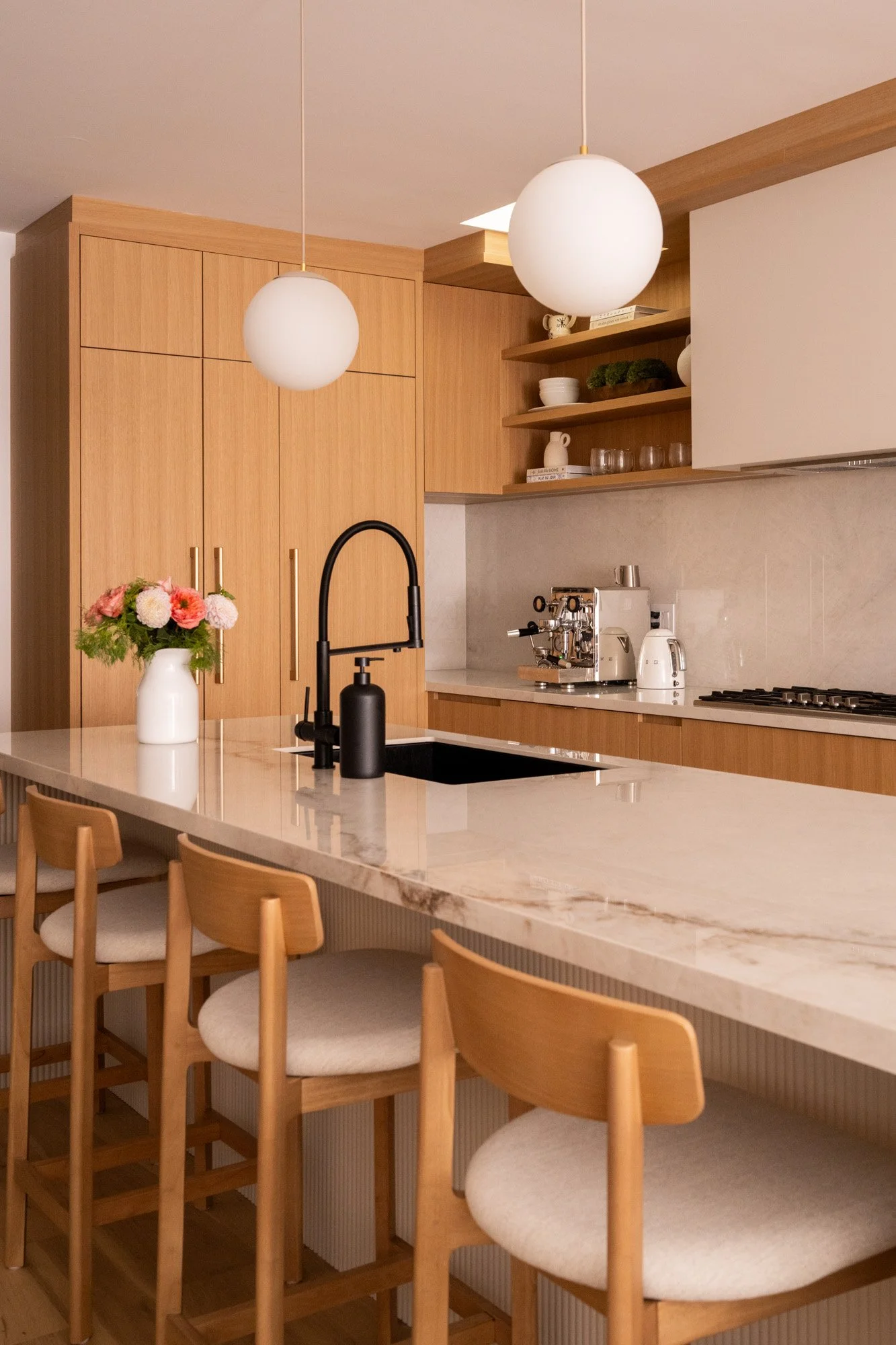 A vase of flowers sit on top of a large reeded kitchen island.