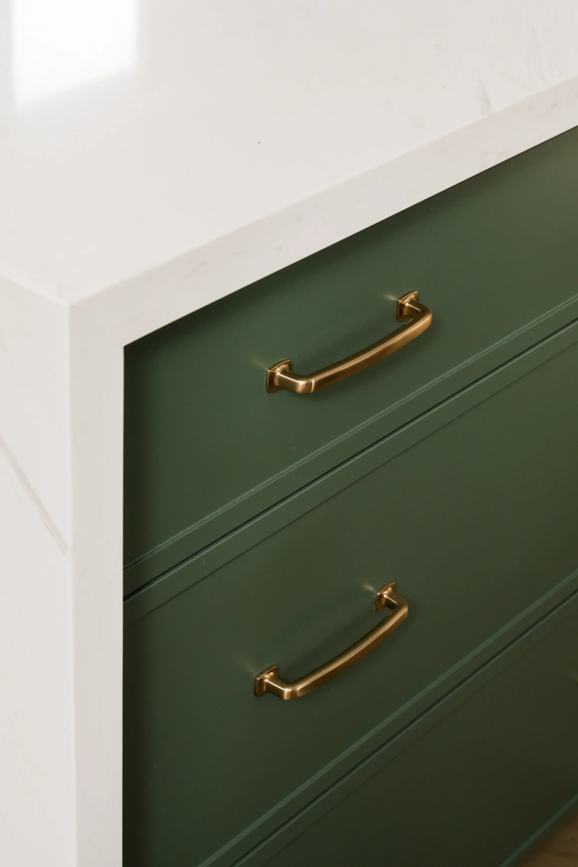 A white kitchen island with green cabinets and gold hardware.