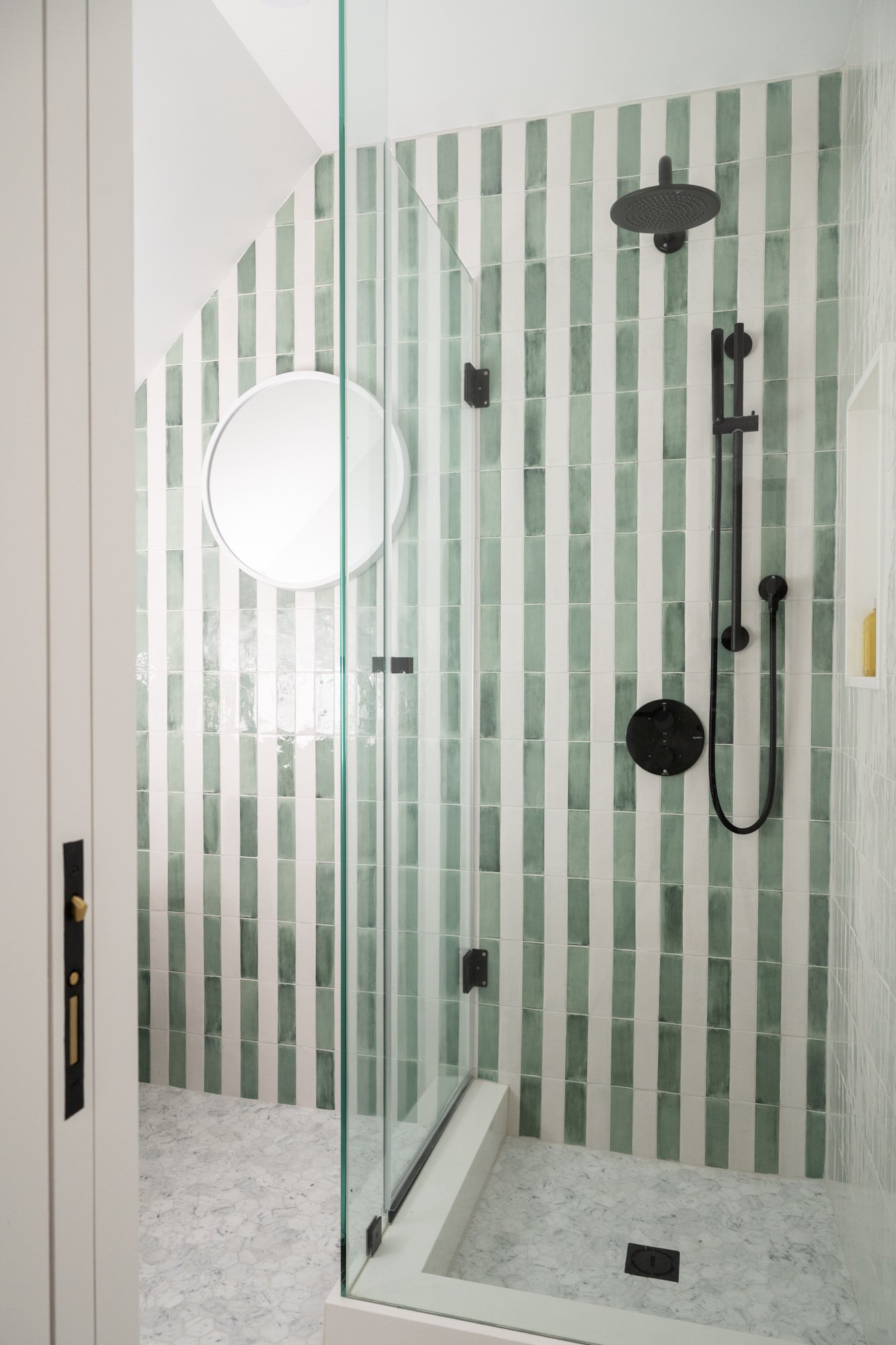 A standing shower with the shower door closed. The wall is tiled with white and green striped pattern