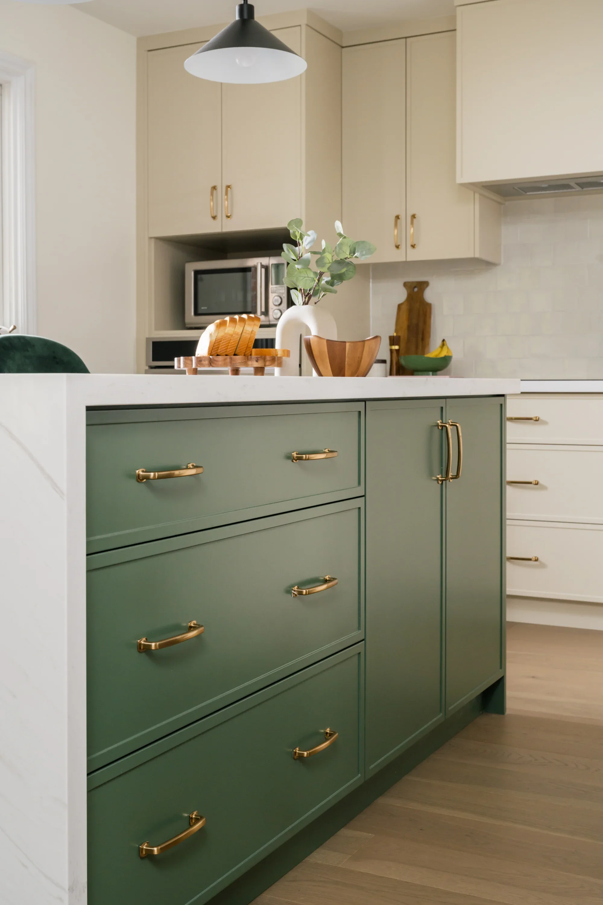 A white kitchen island with green cabinets and gold hardware.