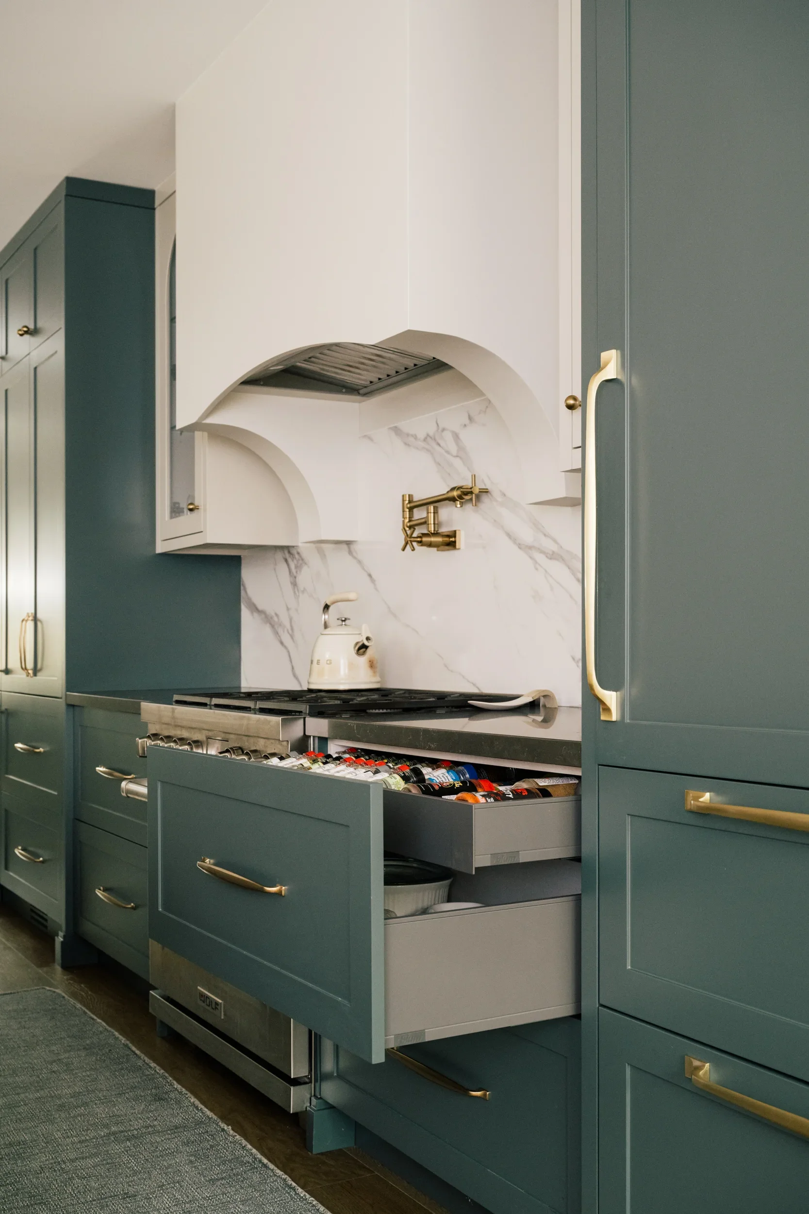 A large cabinet drawer beside the stove is opened, revealing pots inside and a nested drawer of spices.