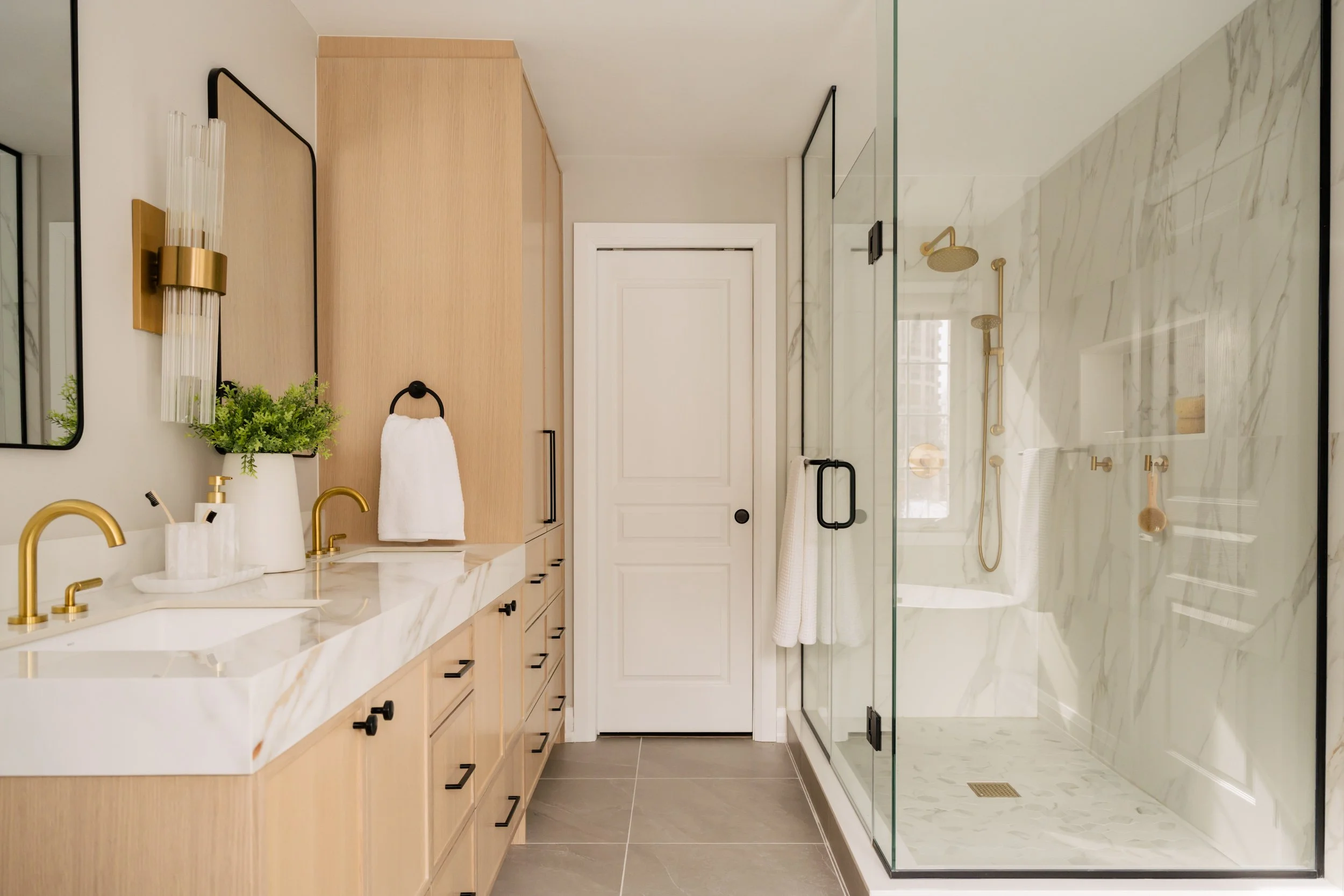 Double vanity and floor to ceiling storage on the left of a bathroom. A large shower encased in glass on the right. The doorway in between.