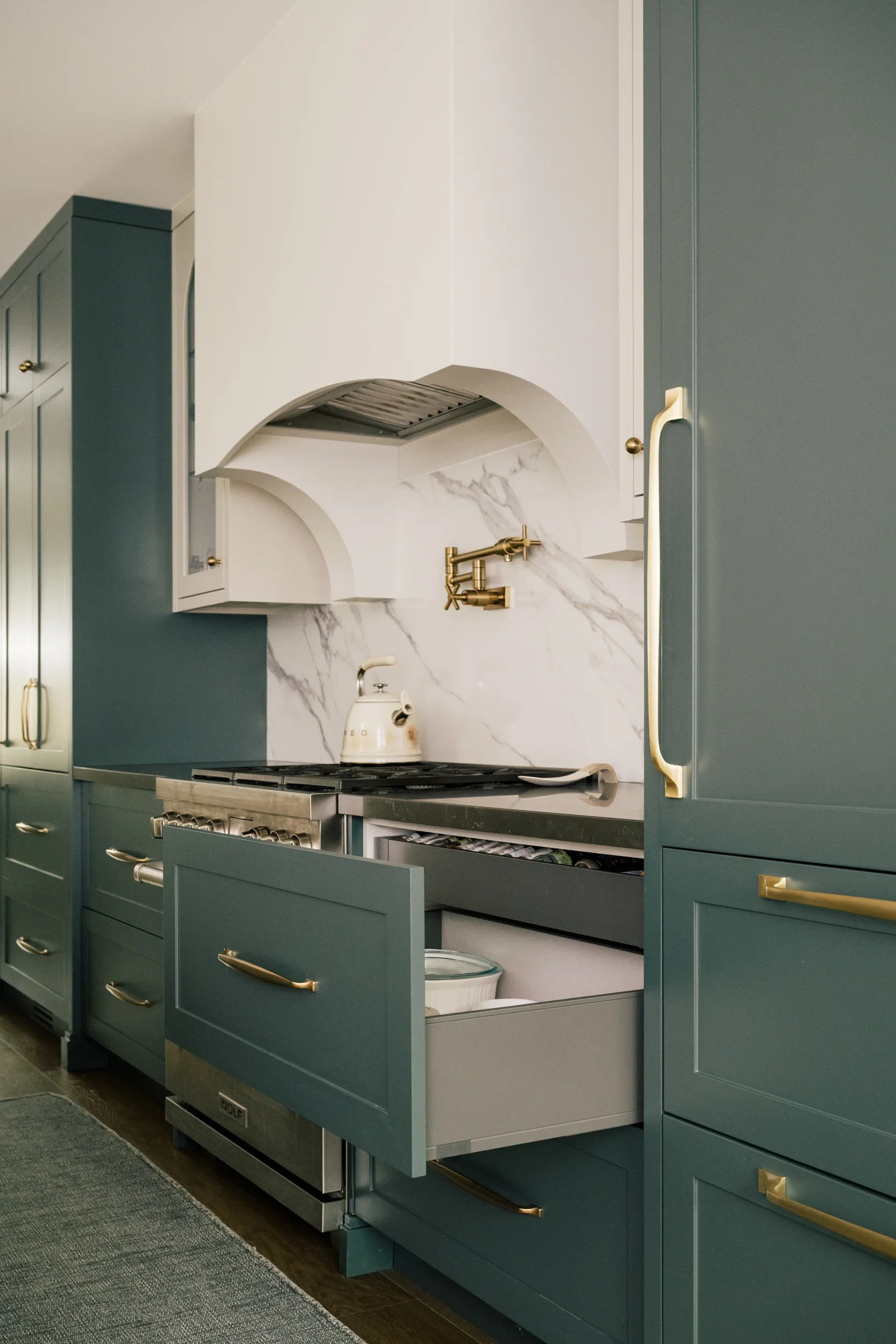 A large cabinet drawer beside the stove is opened revealing pots inside.