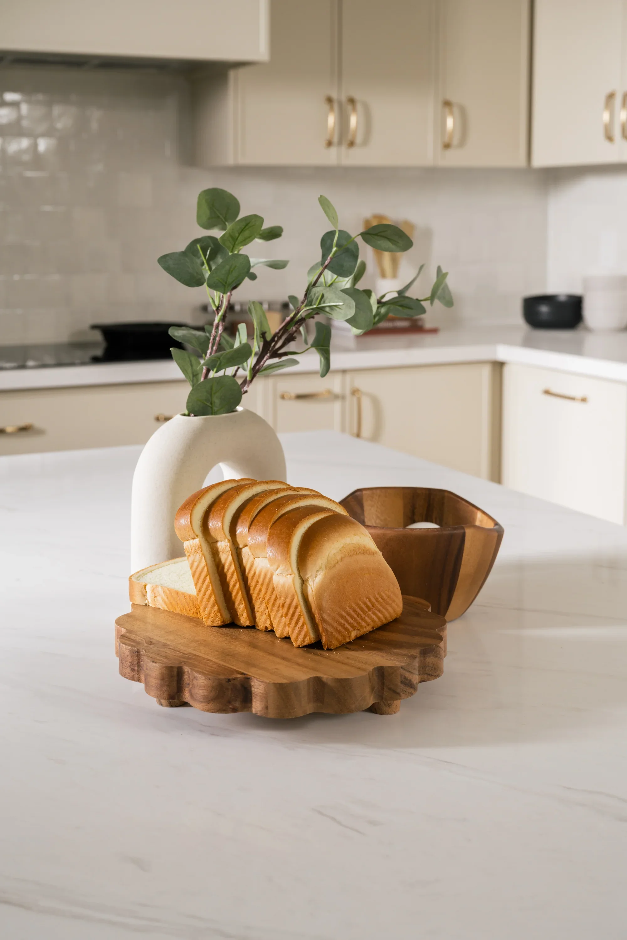 Slices of bread on a wood board beside an arch-shaped vase and another wooden bowl