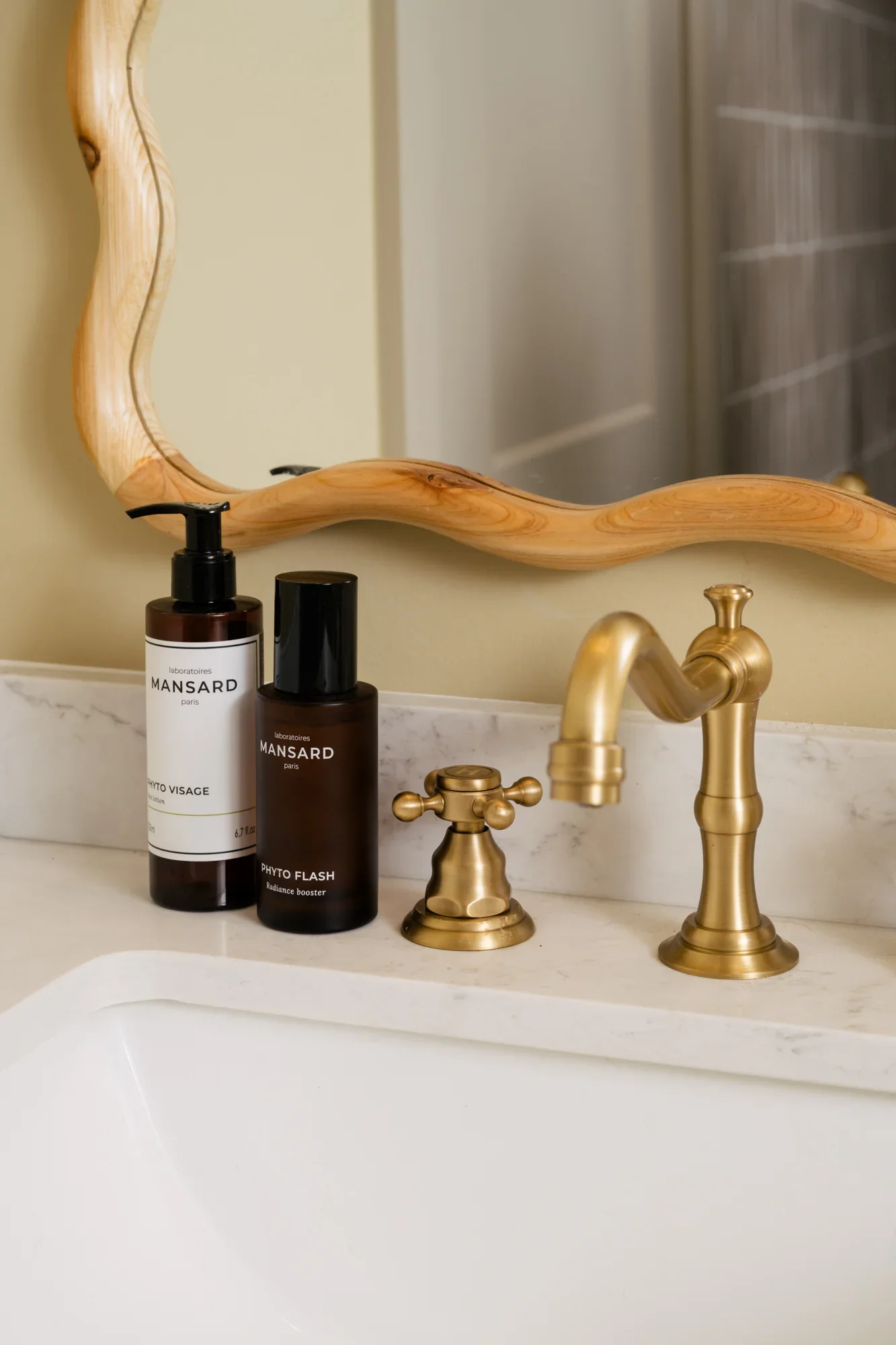 Close up of a brushed gold faucet with soap bottles beside on the countertop.