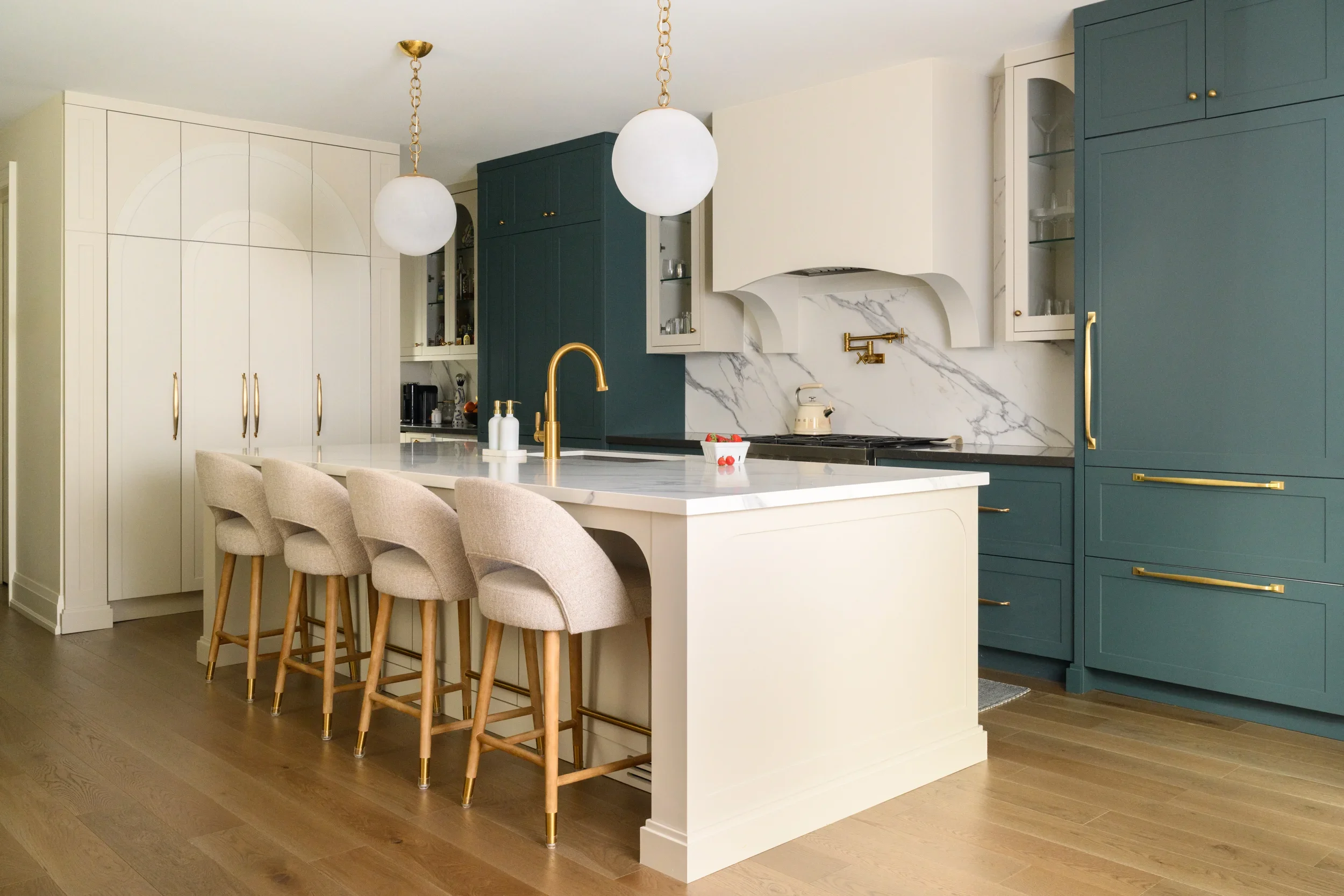 A cream coloured kitchen with muted turquoise cabinets. A large kitchen island sits in the middle with 4 bar stools