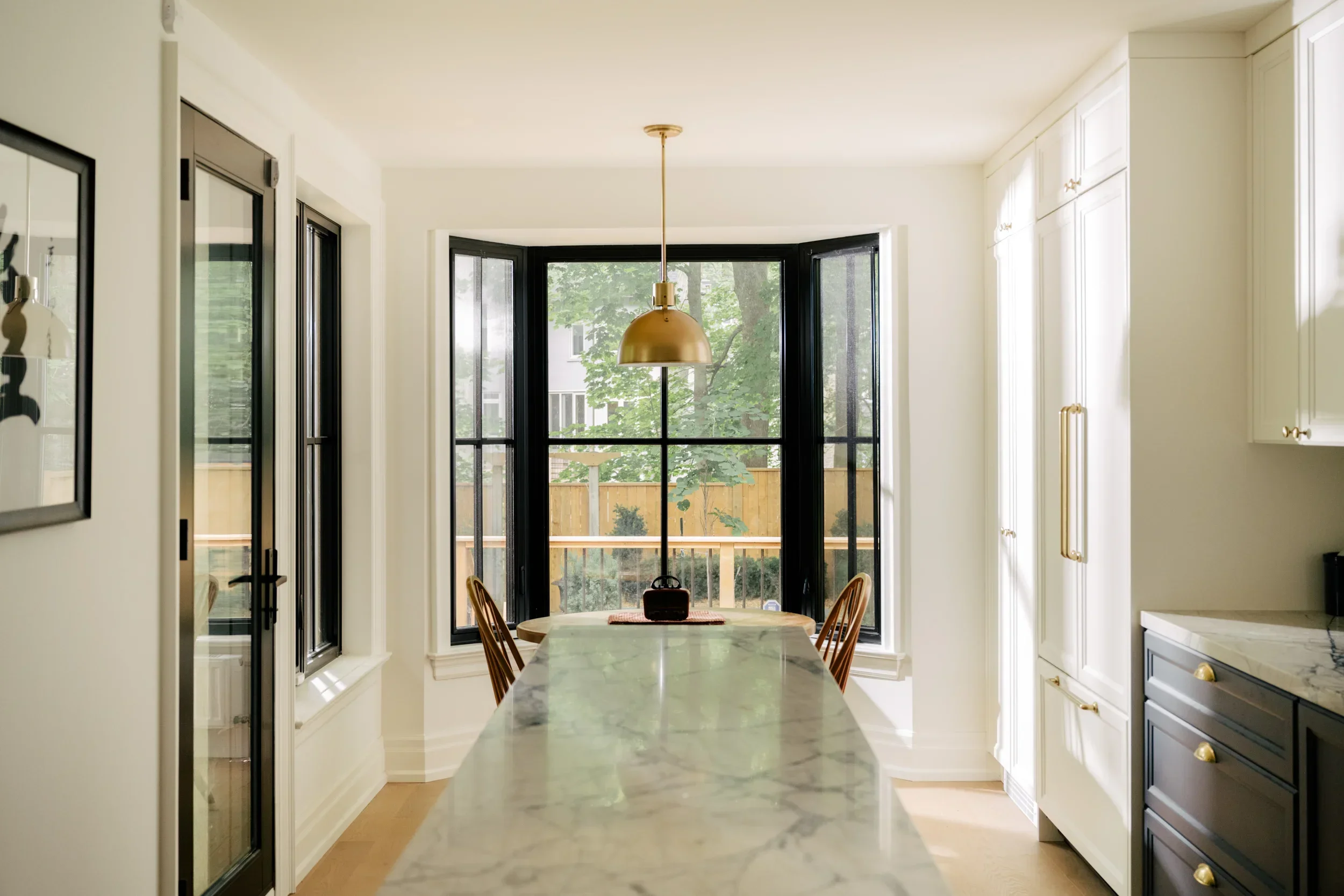 A dining table in front of a bay window at the end of a kitchen with a long island