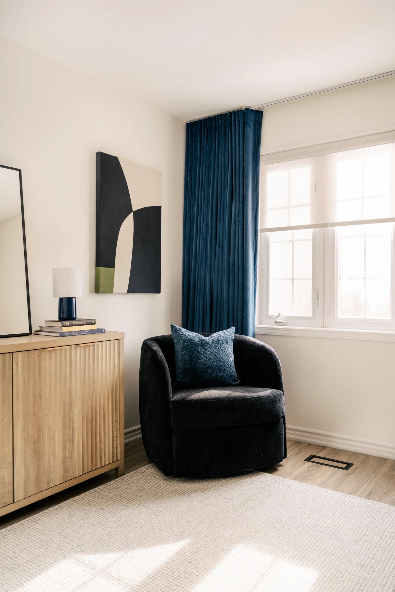 A side chair sits in the corner of a home office with the blackout curtain open and sunlight streaming in.