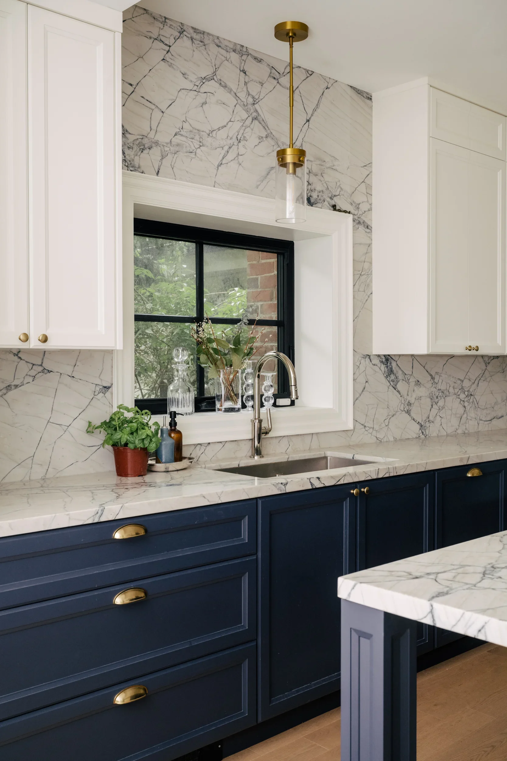 Kitchen sink in front of a window, in a kitchen with navy blue lower cabinets and white upper cabinets.