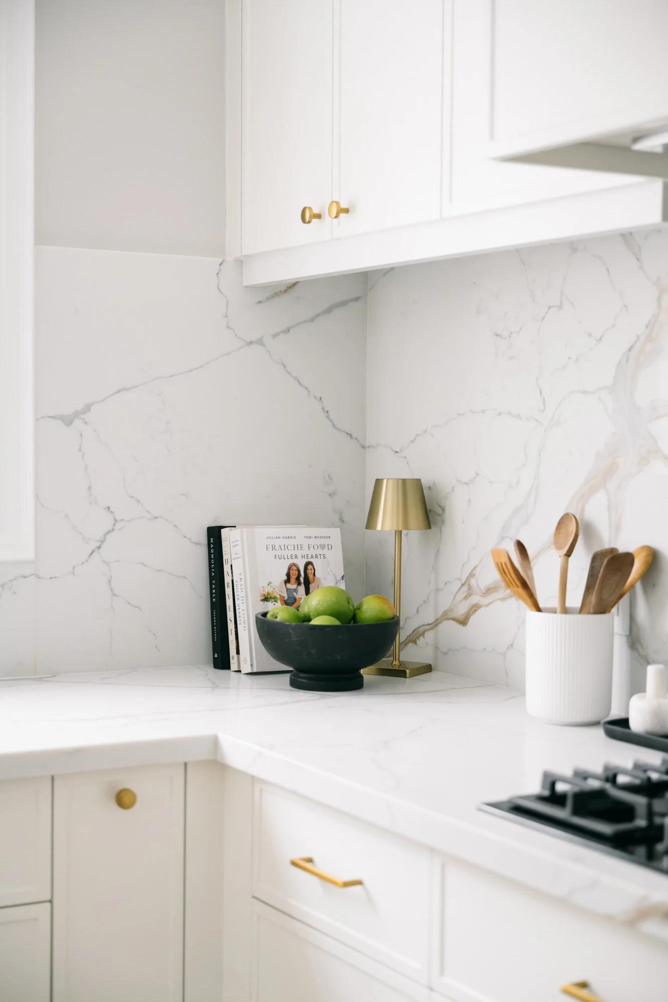 The corner of a kitchen countertop with cookbooks, apples in a bowl and a small tabletop lamp.