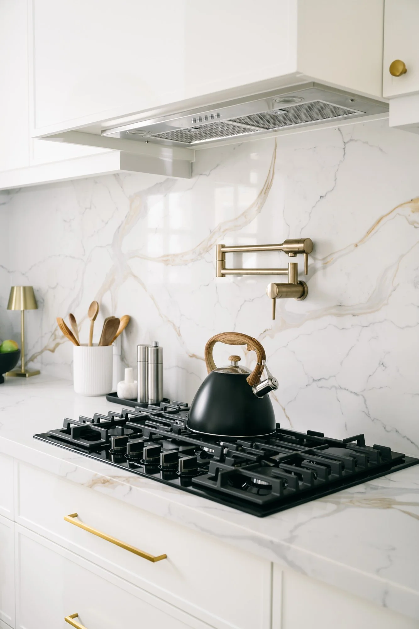 A black kettle sits on a gas stove with a marbled backsplash