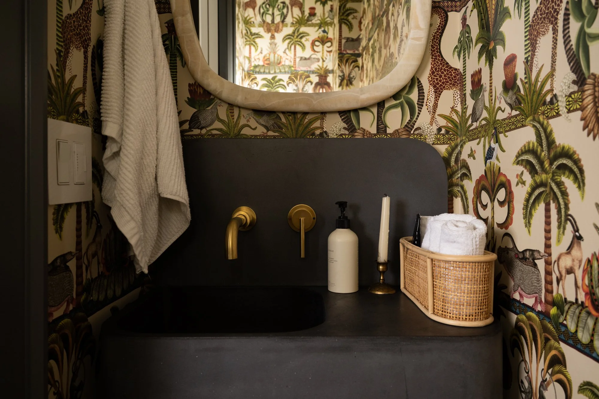 Powder room with dark grey concrete sink and gold hardware. The entire powder room is covered in animal print wallpaper.