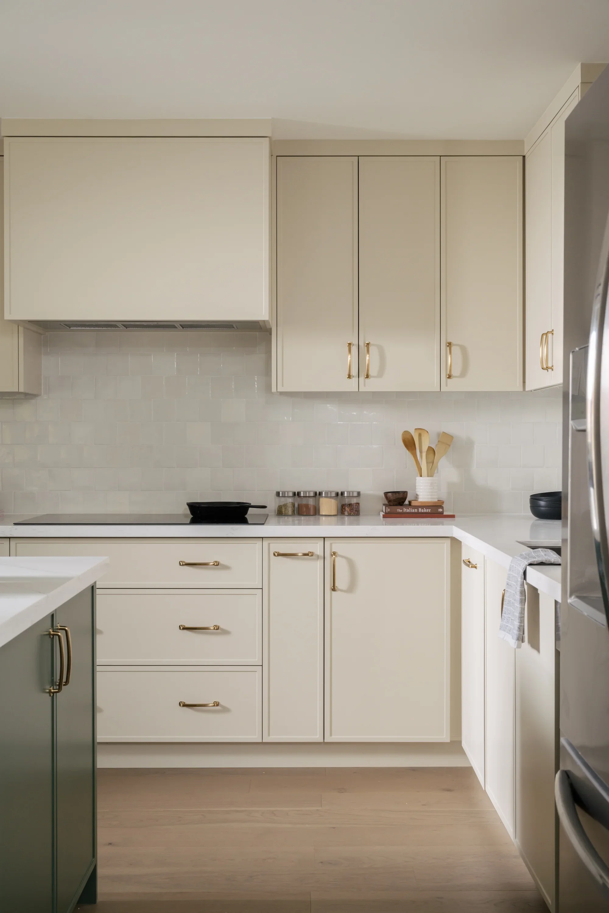 A cream-coloured kitchen with spice jars on the countertop and wooden utensils. A cast iron pan is on the glass stove.
