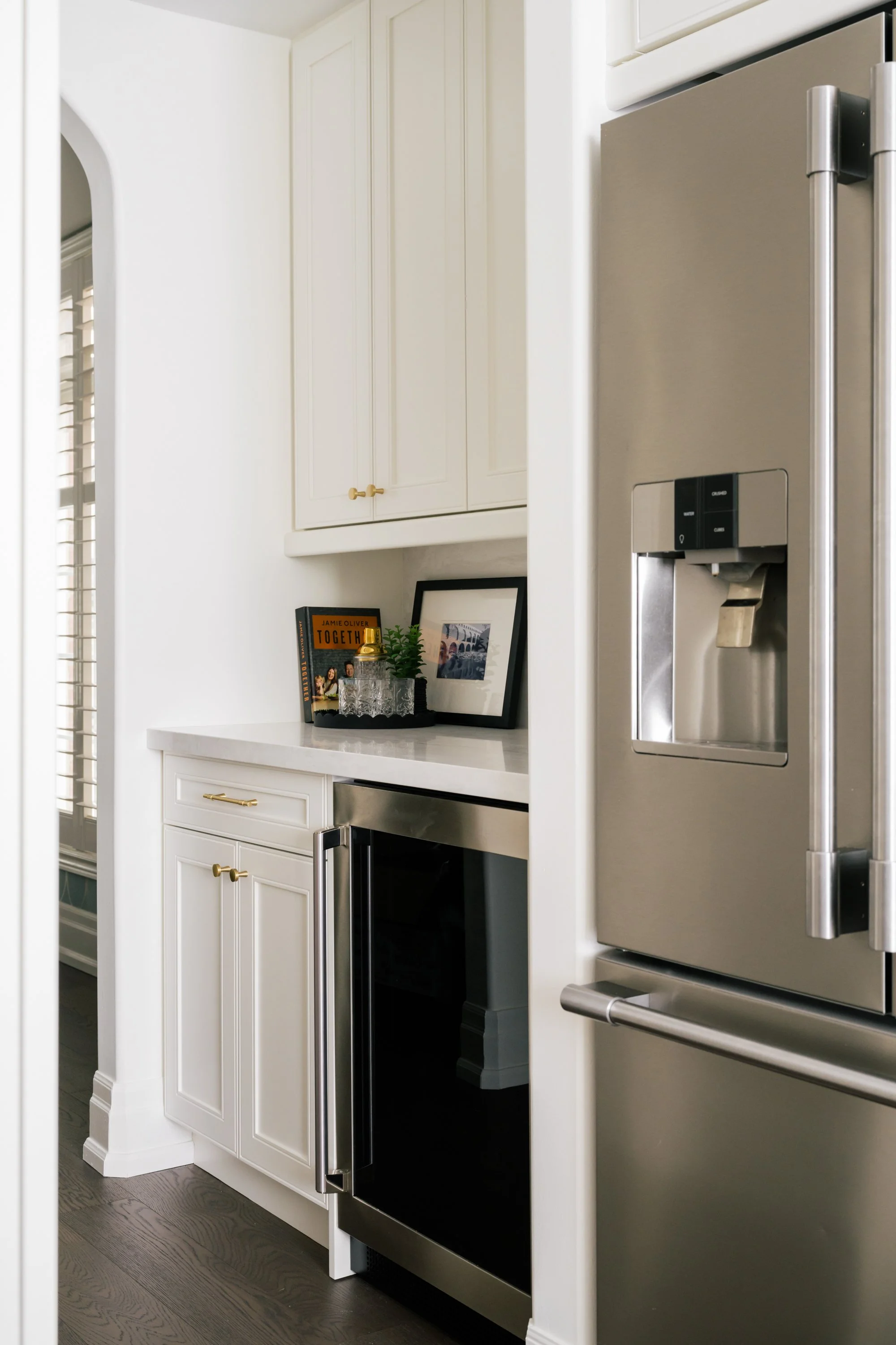 A drinks station stands beside a fridge. A wine cooler sits in the bottom cabinet