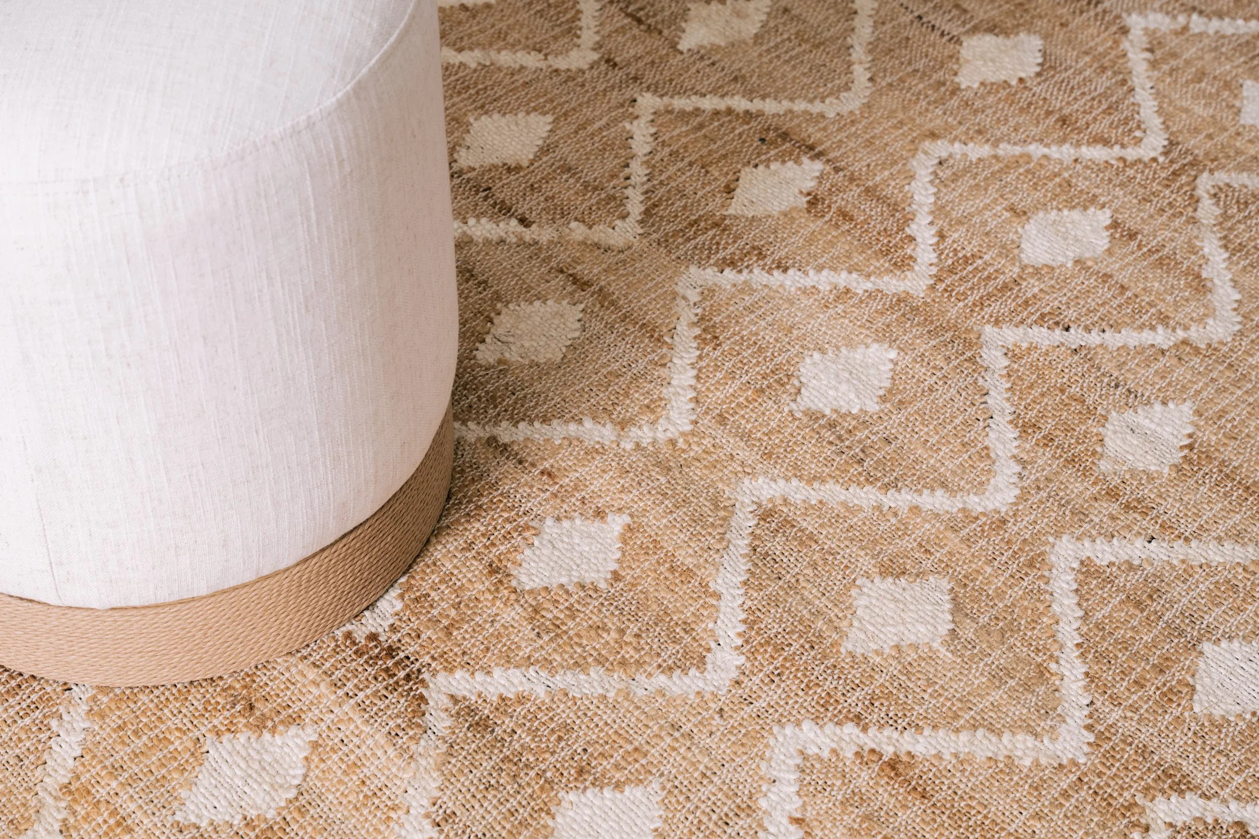 A round white ottoman sits on top of a patterned rug.