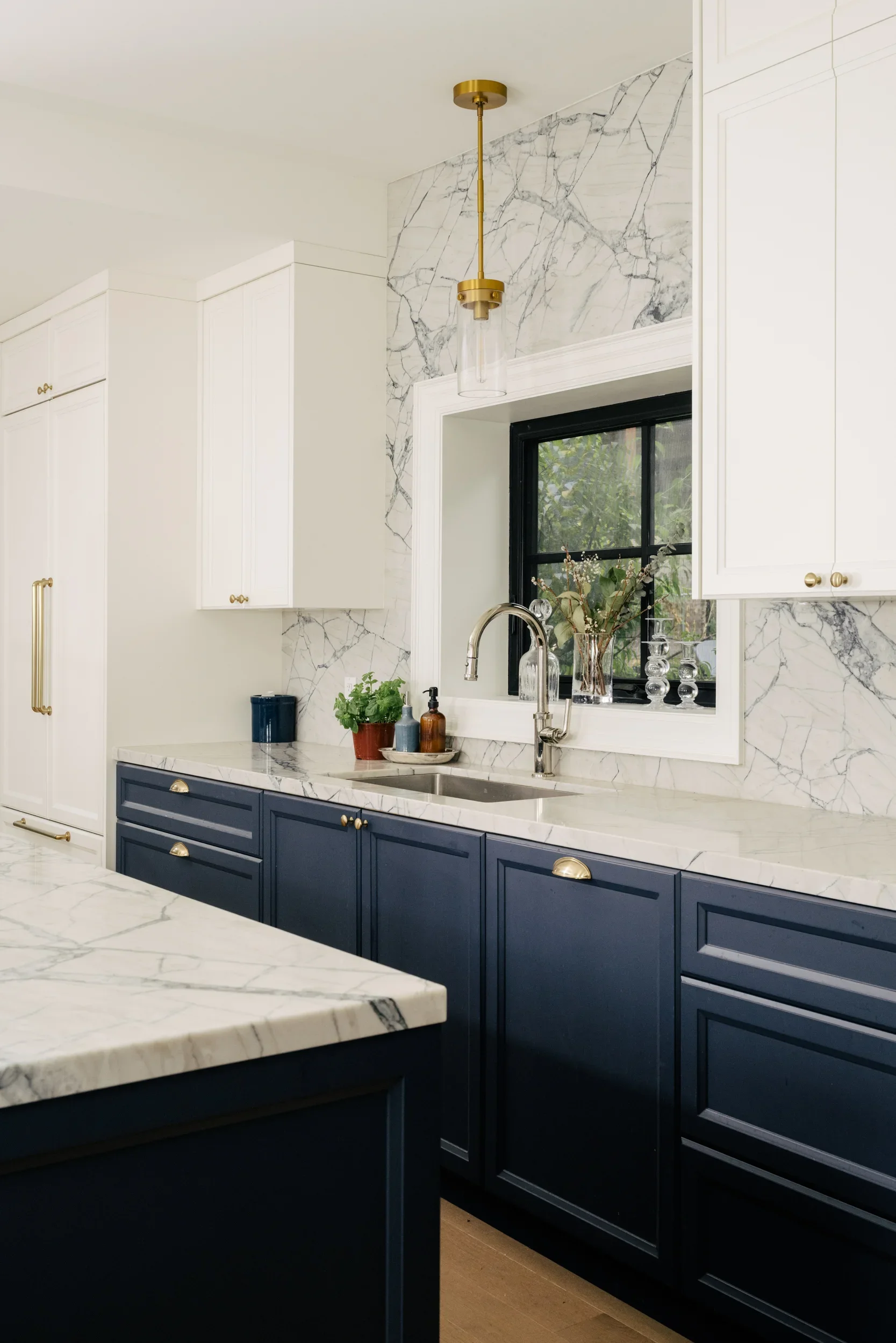 Kitchen sink in front of a window, in a kitchen with navy blue lower cabinets and white upper cabinets.