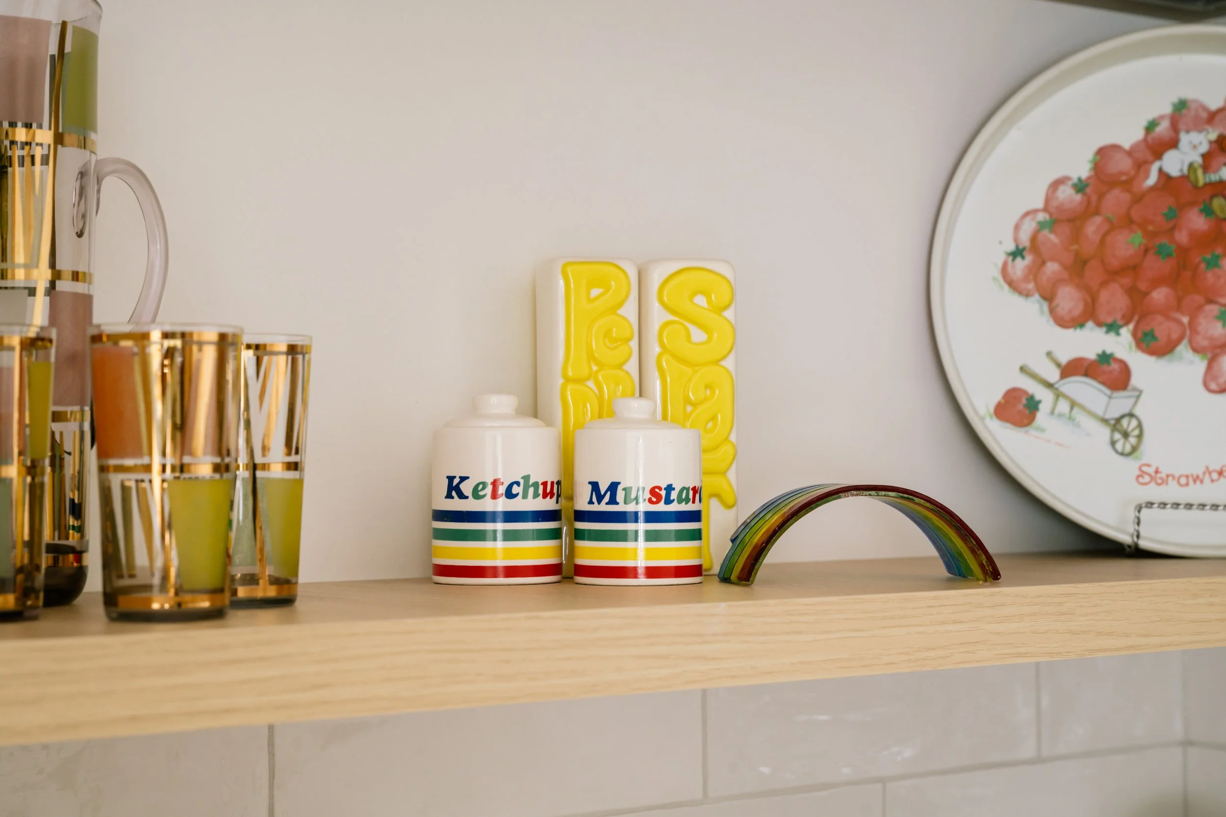 A close up of vintage kitchen items on a shelf. A pair of jars labeled ketchup and mustard with coloured stripes.