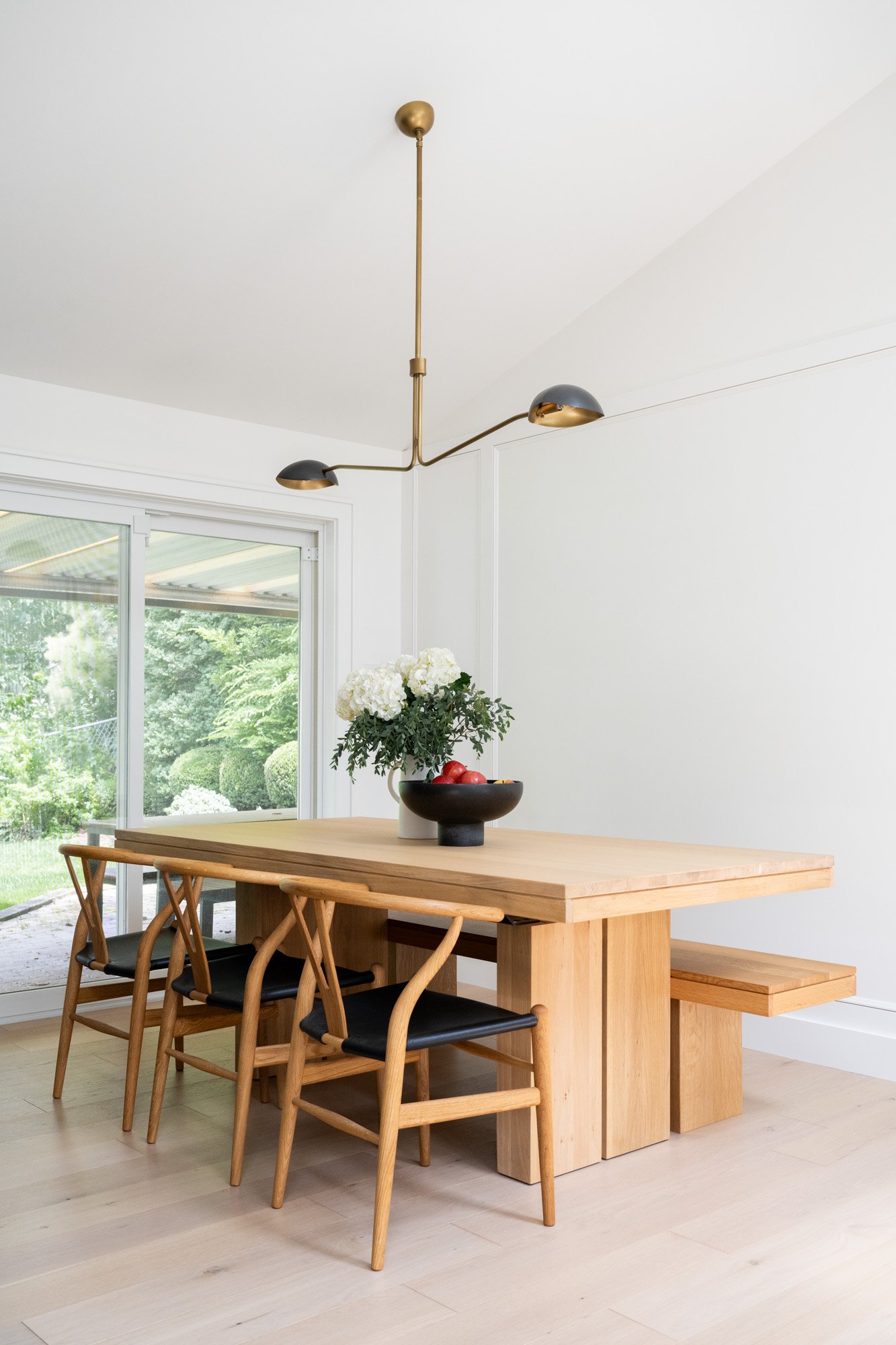 A large wooden dining table with 3 chairs and a bench, styled with a bowl of red apples and fresh hydrangeas.