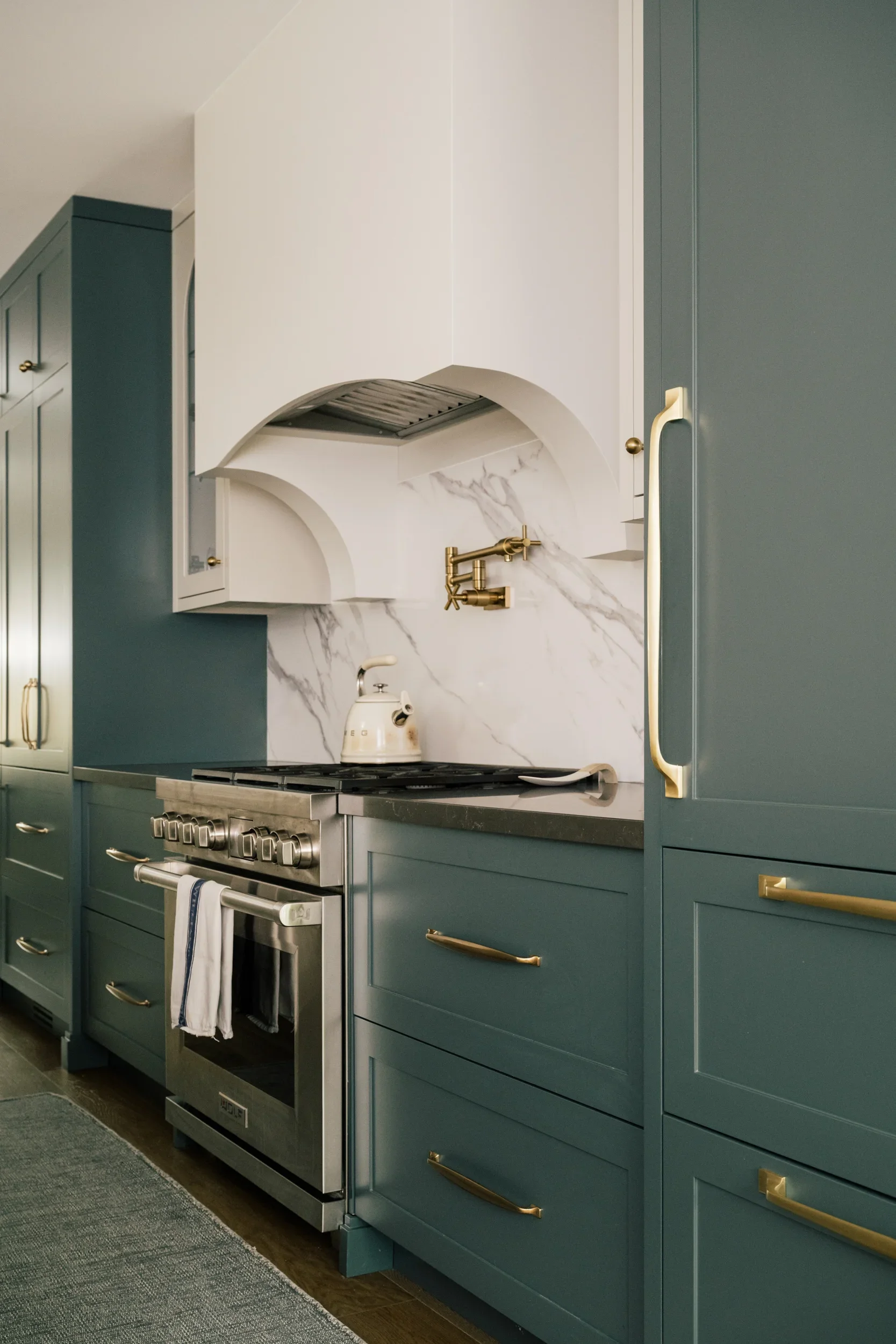 A view of a large gas stove and gold potfiller on the wall. A Smeg kettle sits on the stove.