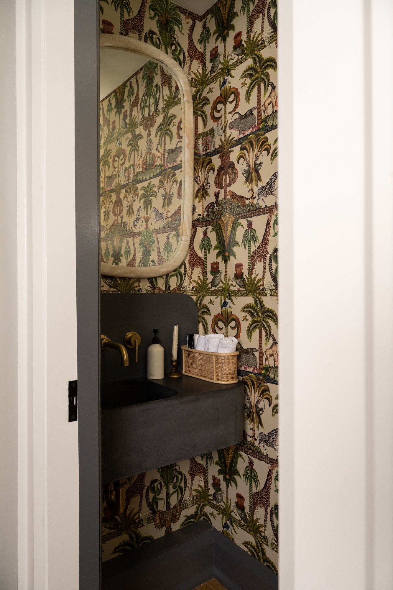 Powder room with dark grey concrete sink and gold hardware. The entire powder room is covered in animal print wallpaper.