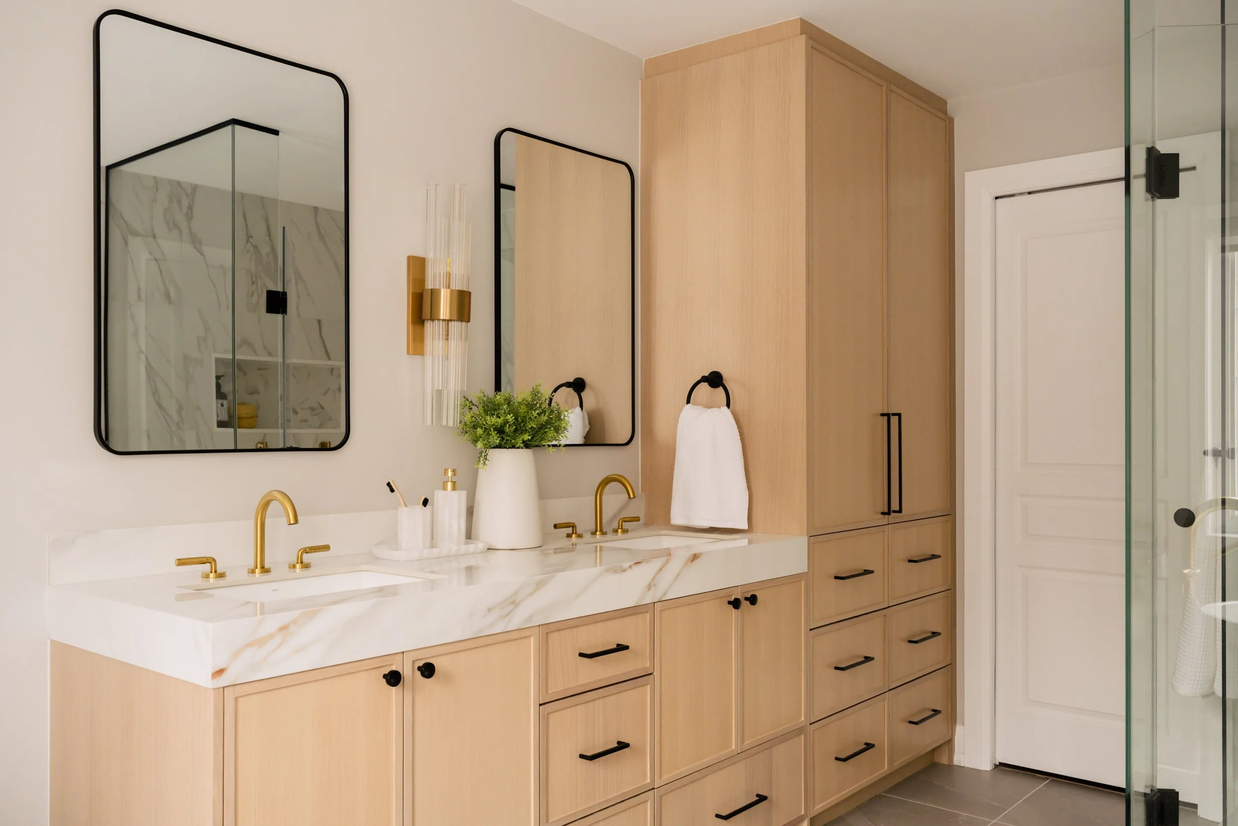 A 45-degree angle view of a double vanity made of warm wood and floor to ceiling cabinets in the ceiling.