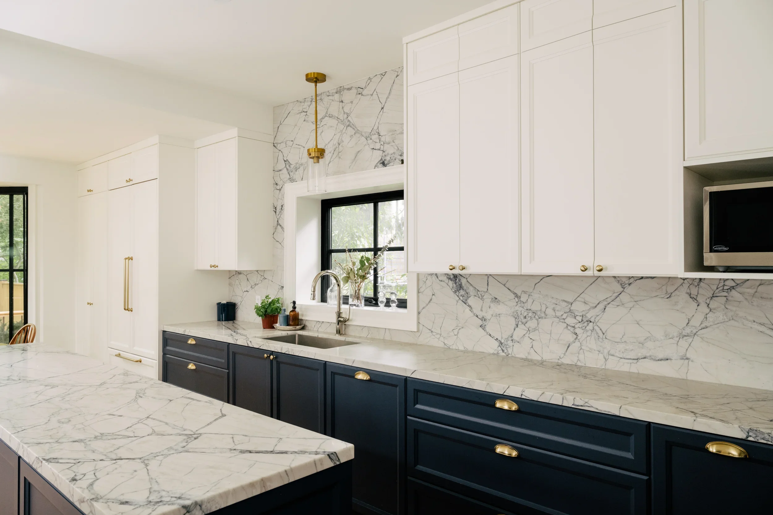 A long kitchen with marble backsplash and navy blue lower kitchen cabinets and gold handle pulls